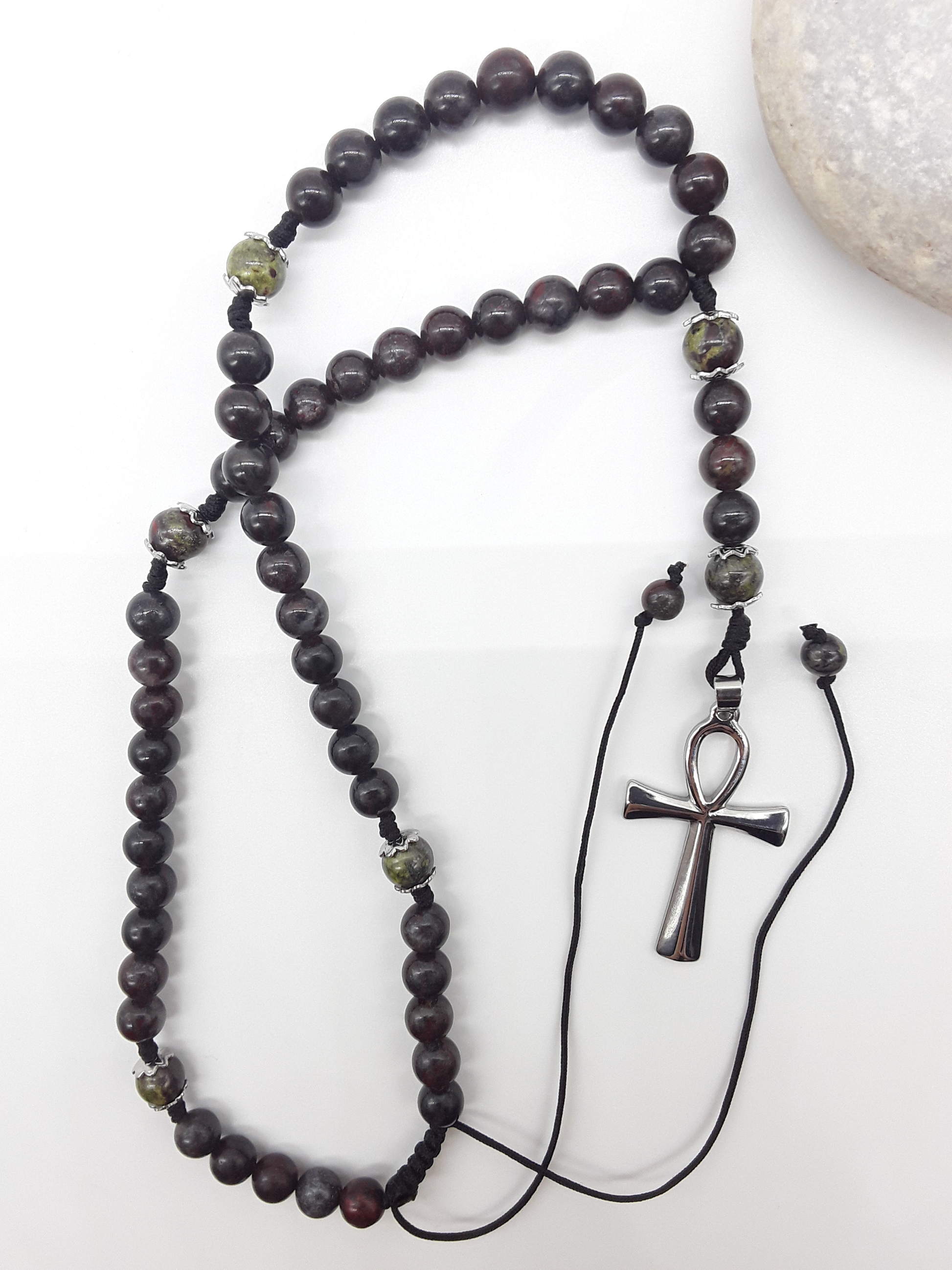 Catholic bloodstone rosary with Ankh cross placed beside natural stone on white surface
