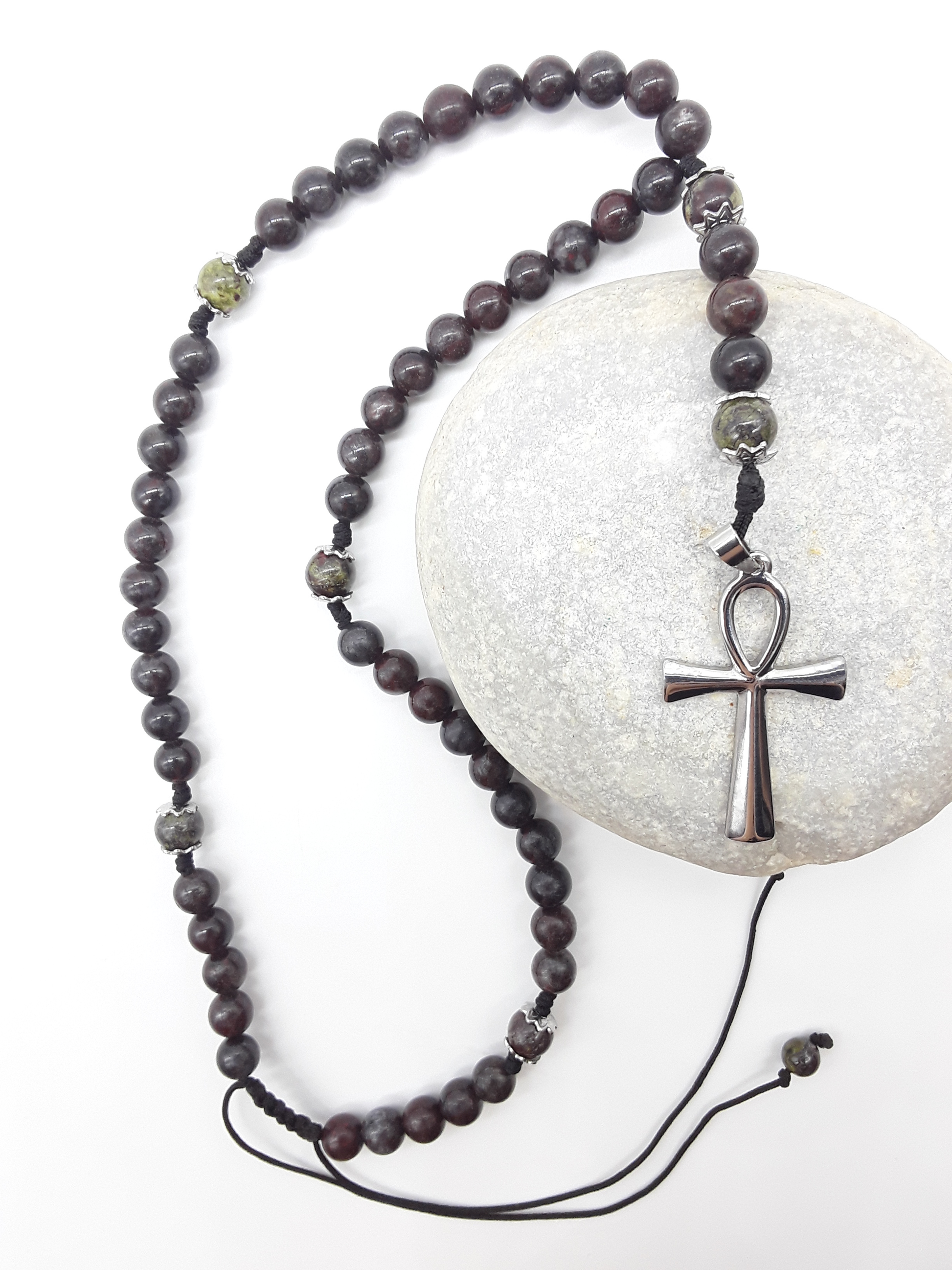 Catholic bloodstone rosary with Ankh cross placed beside natural stone on white surface