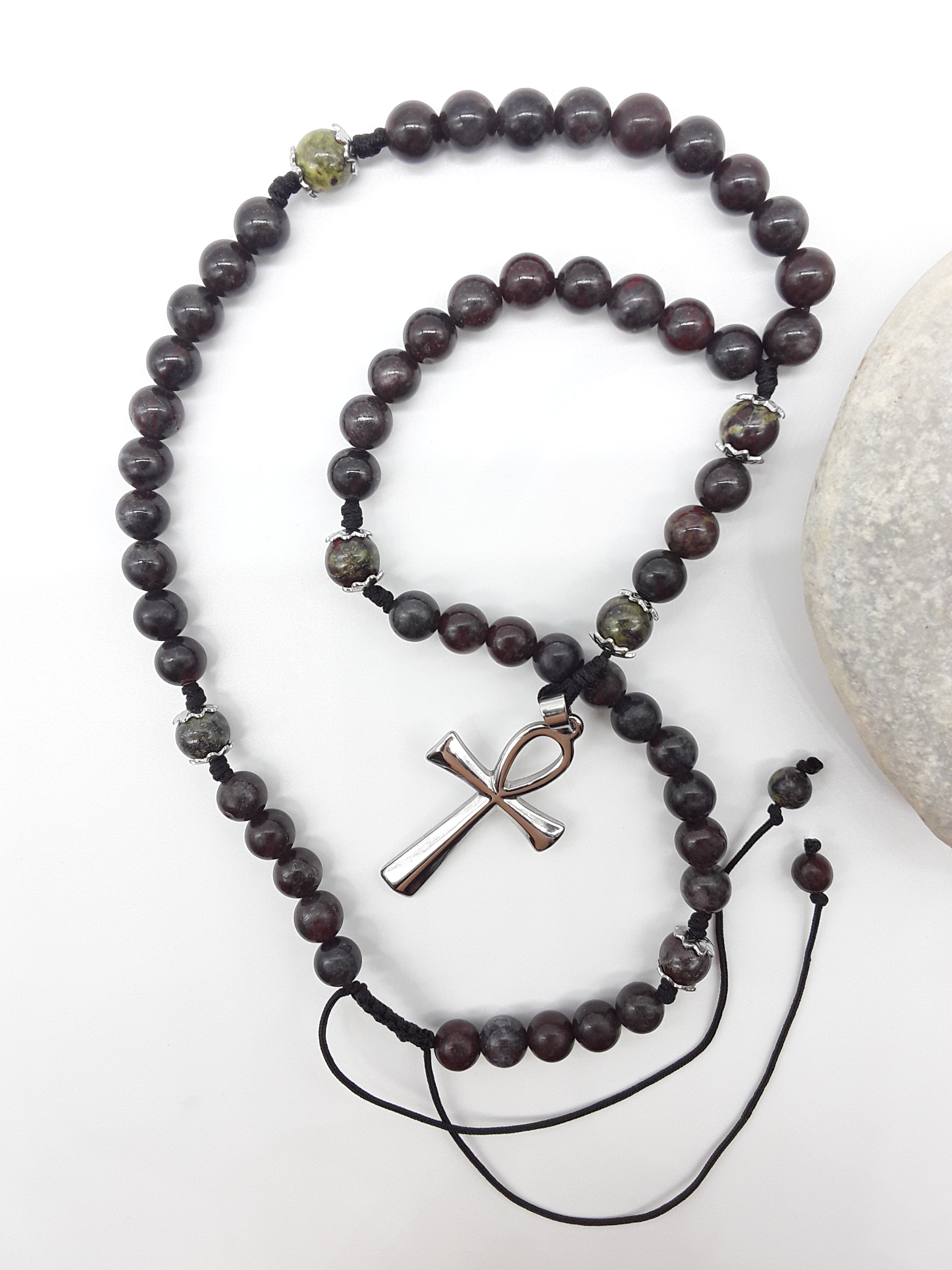 Catholic bloodstone rosary with Ankh cross placed beside natural stone on white surface