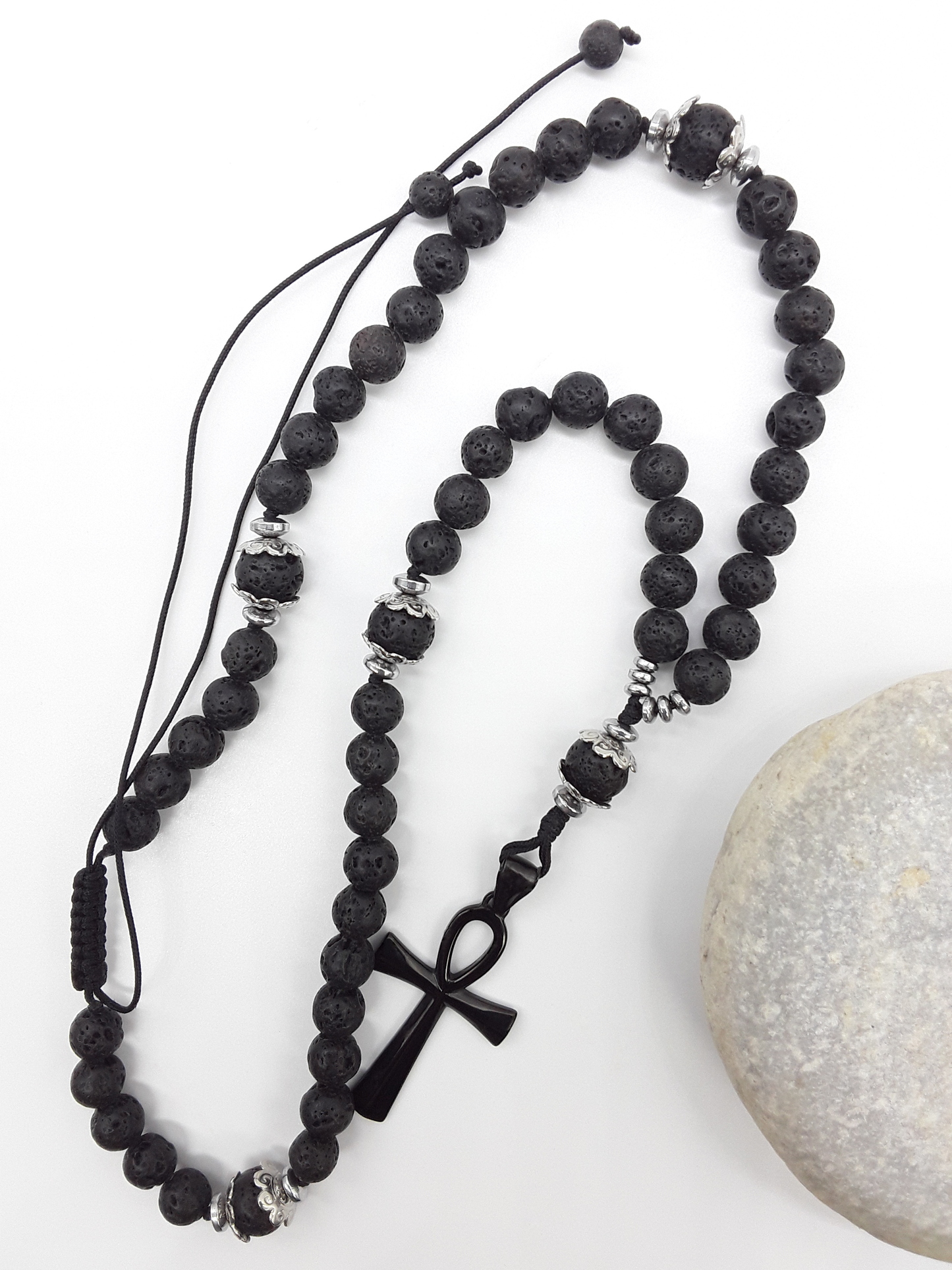 Lava and steel Orthodox Rosary with black Ankh cross and adjustable cord beside natural stone surface by Polmadeva.
