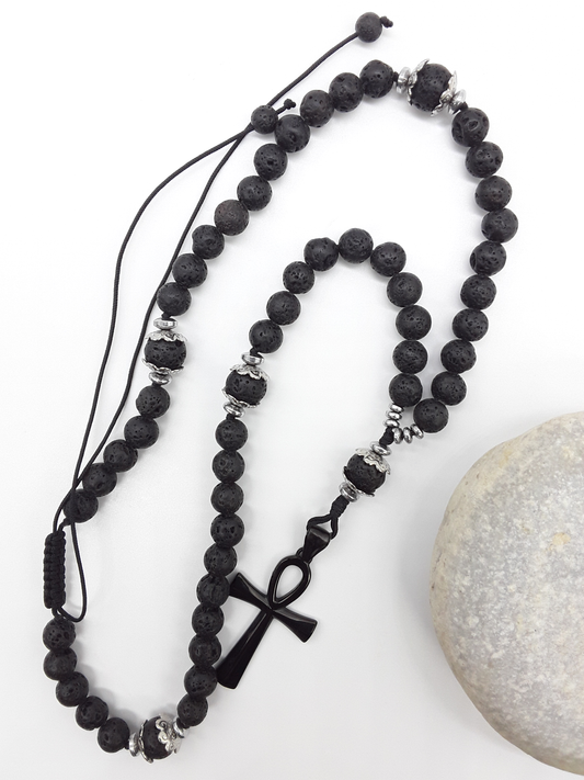 Lava and steel Orthodox Rosary with black Ankh cross and adjustable cord beside natural stone surface by Polmadeva.