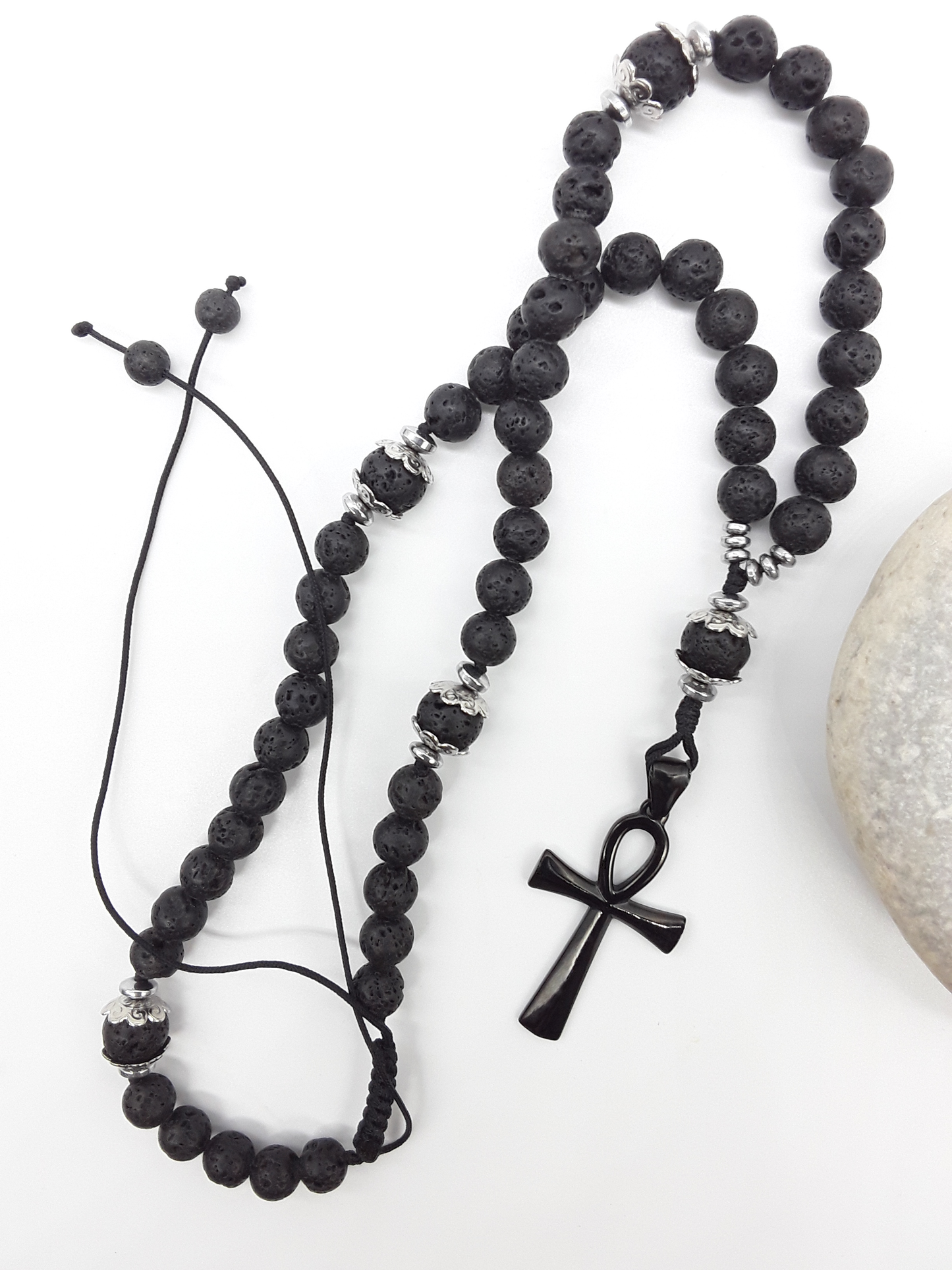 Lava and steel Orthodox Rosary with black Ankh cross and adjustable cord beside natural stone surface by Polmadeva.