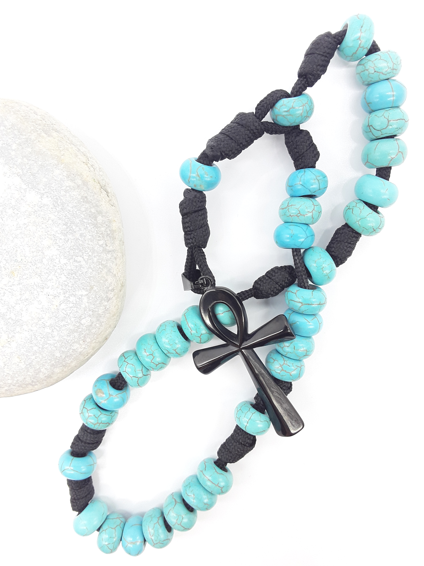 The Living Covenant Paracord Anglican Prayer Beads by Polmadeva beside natural stone, featuring Turquoise and Ankh cross
