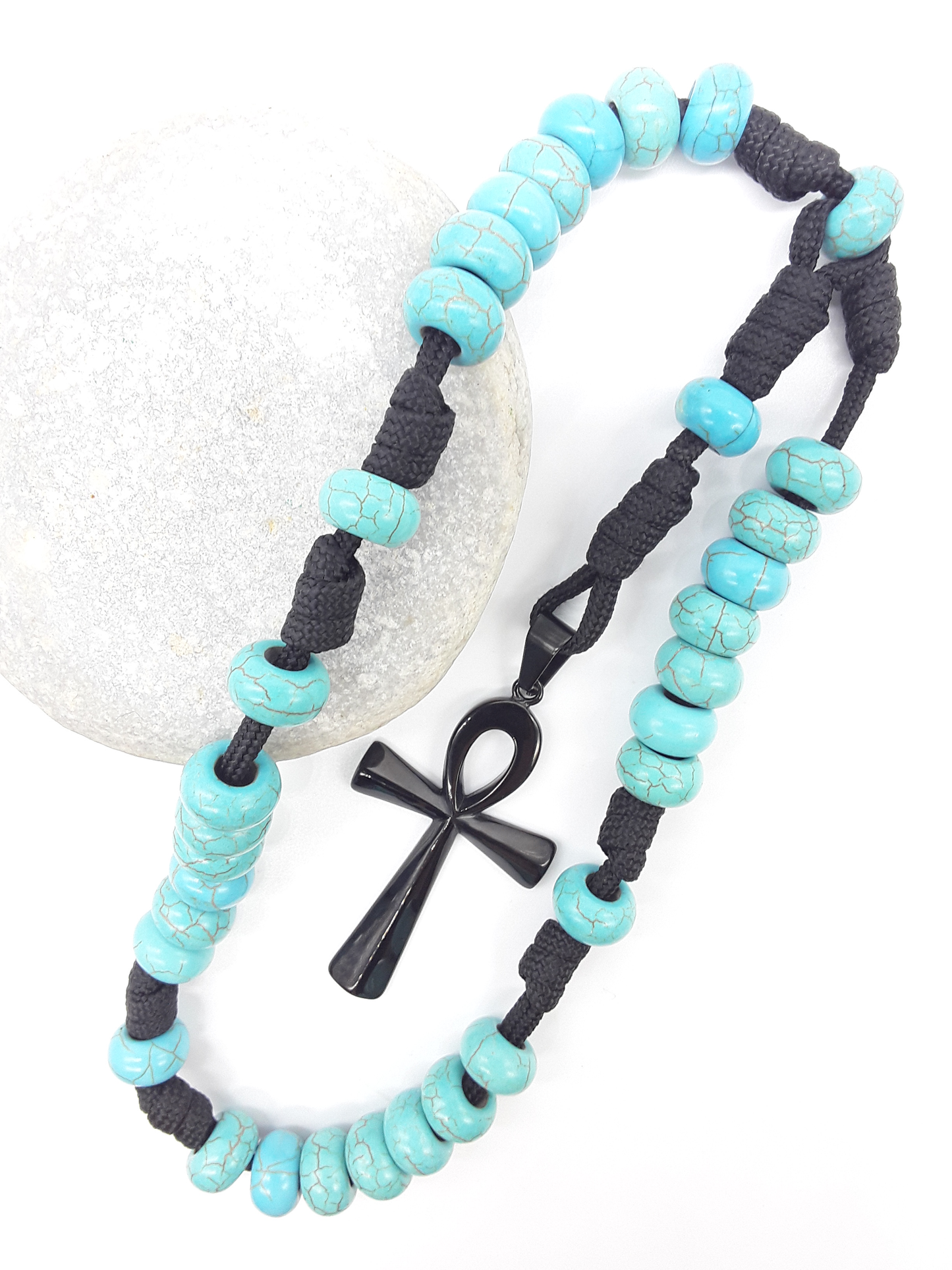 The Living Covenant Paracord Anglican Prayer Beads by Polmadeva placed on stone, crafted with Turquoise and stainless steel Ankh cross