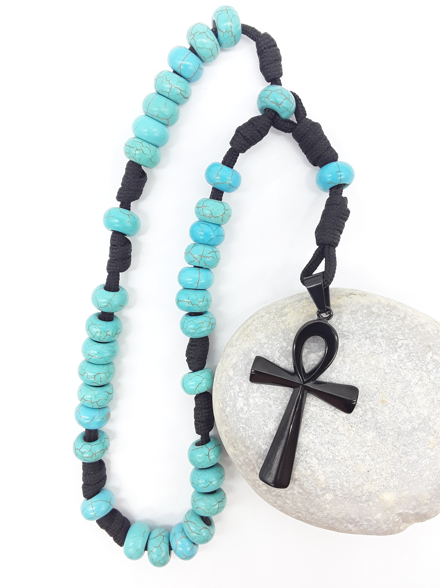 The Living Covenant Paracord Anglican Prayer Beads by Polmadeva placed on stone, crafted with Turquoise and stainless steel Ankh cross