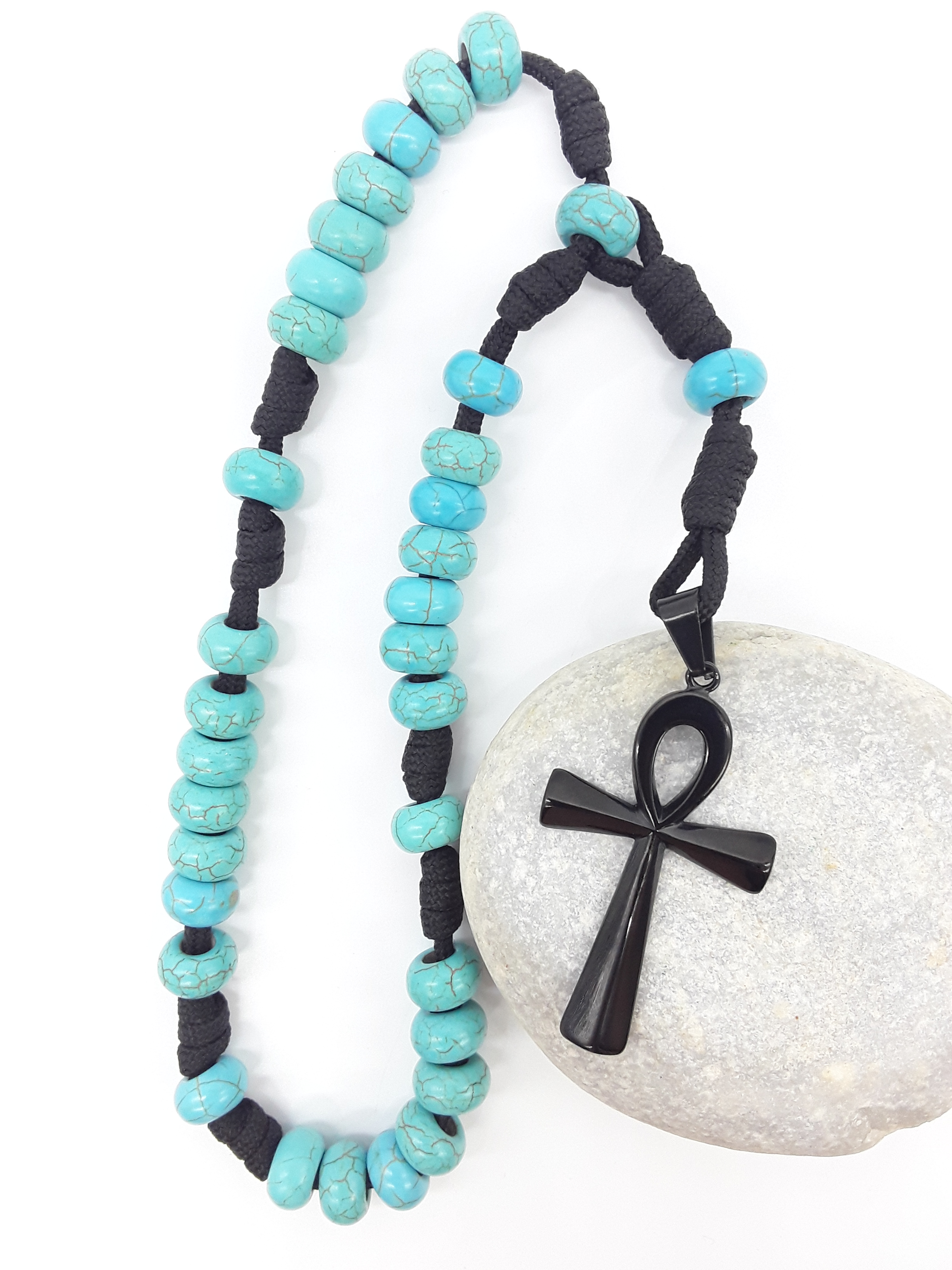 The Living Covenant Paracord Anglican Prayer Beads by Polmadeva placed on stone, crafted with Turquoise and stainless steel Ankh cross