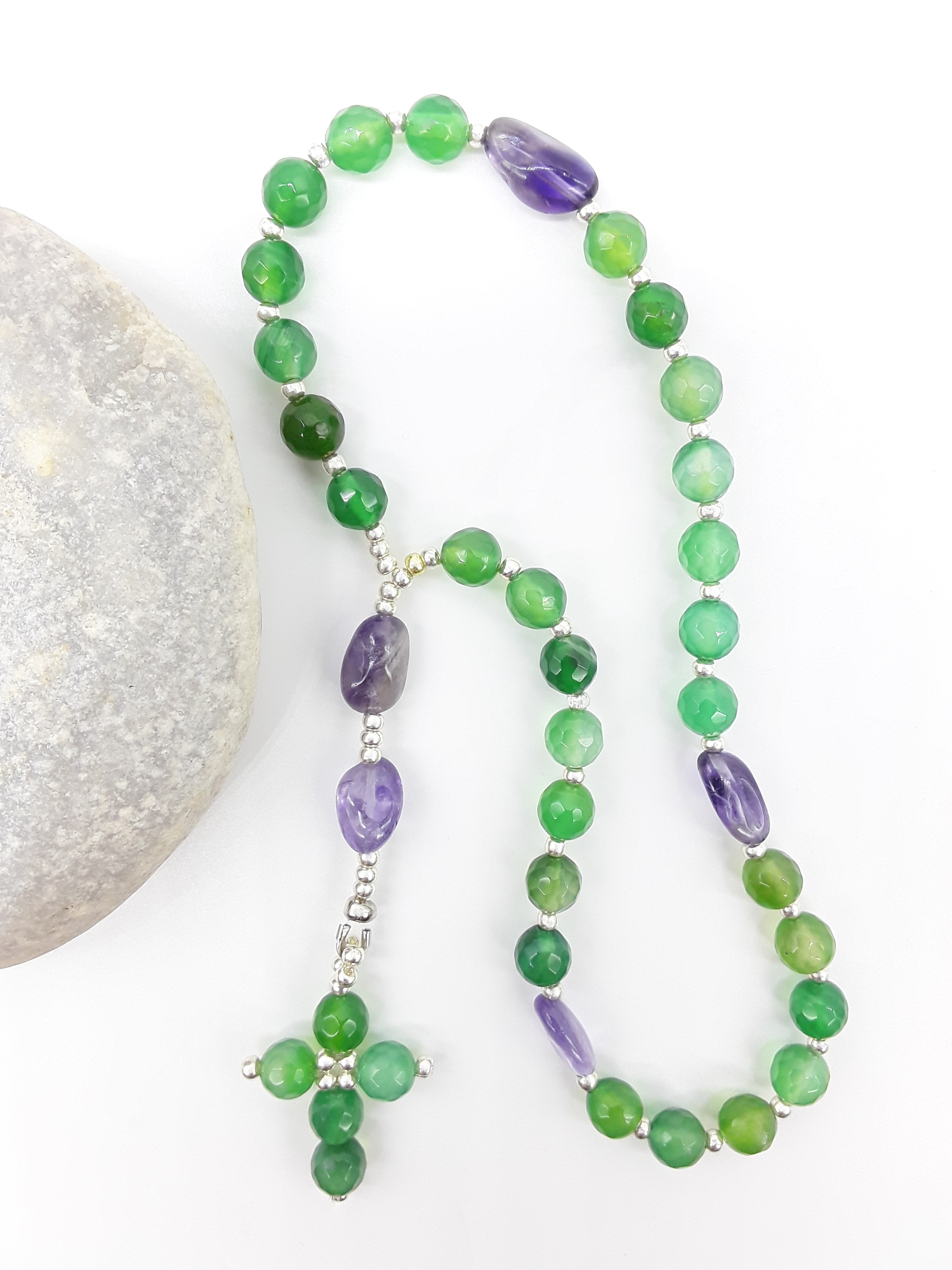 The Living Garden Anglican Prayer Beads by Polmadeva beside natural stone, featuring green Agate, Amethyst, and Miyuki details