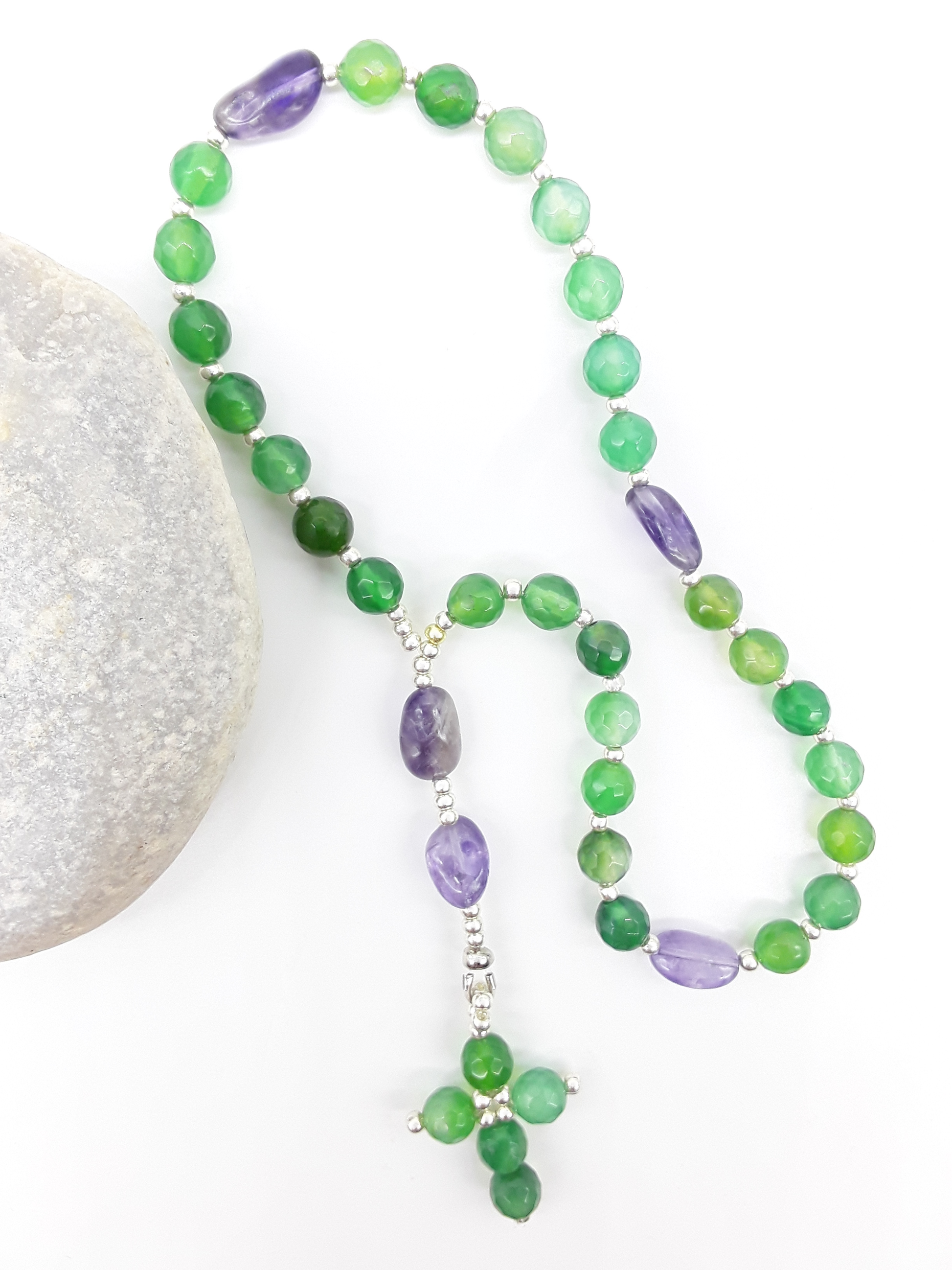 The Living Garden Anglican Prayer Beads by Polmadeva beside natural stone, featuring green Agate, Amethyst, and Miyuki details