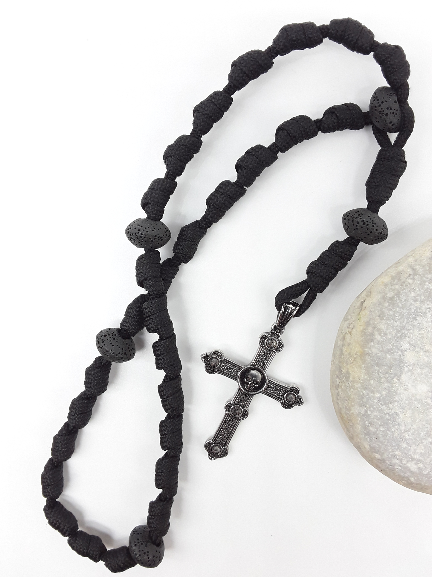 The Living Memory Paracord Anglican Prayer Beads by Polmadeva beside natural stone, featuring Volcanic Lava Stones and Skull Cross