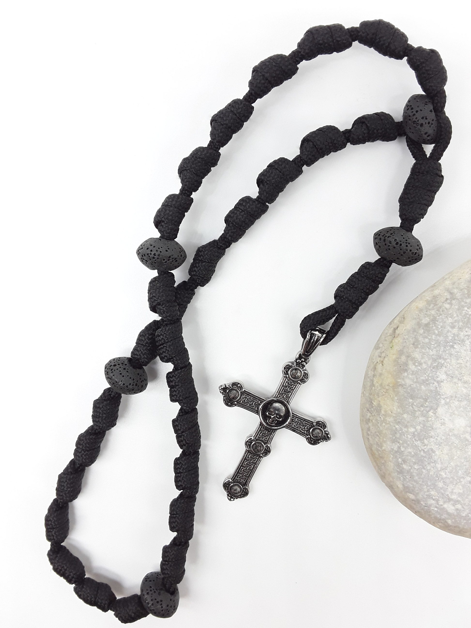 The Living Memory Paracord Anglican Prayer Beads by Polmadeva beside natural stone, featuring Volcanic Lava Stones and Skull Cross