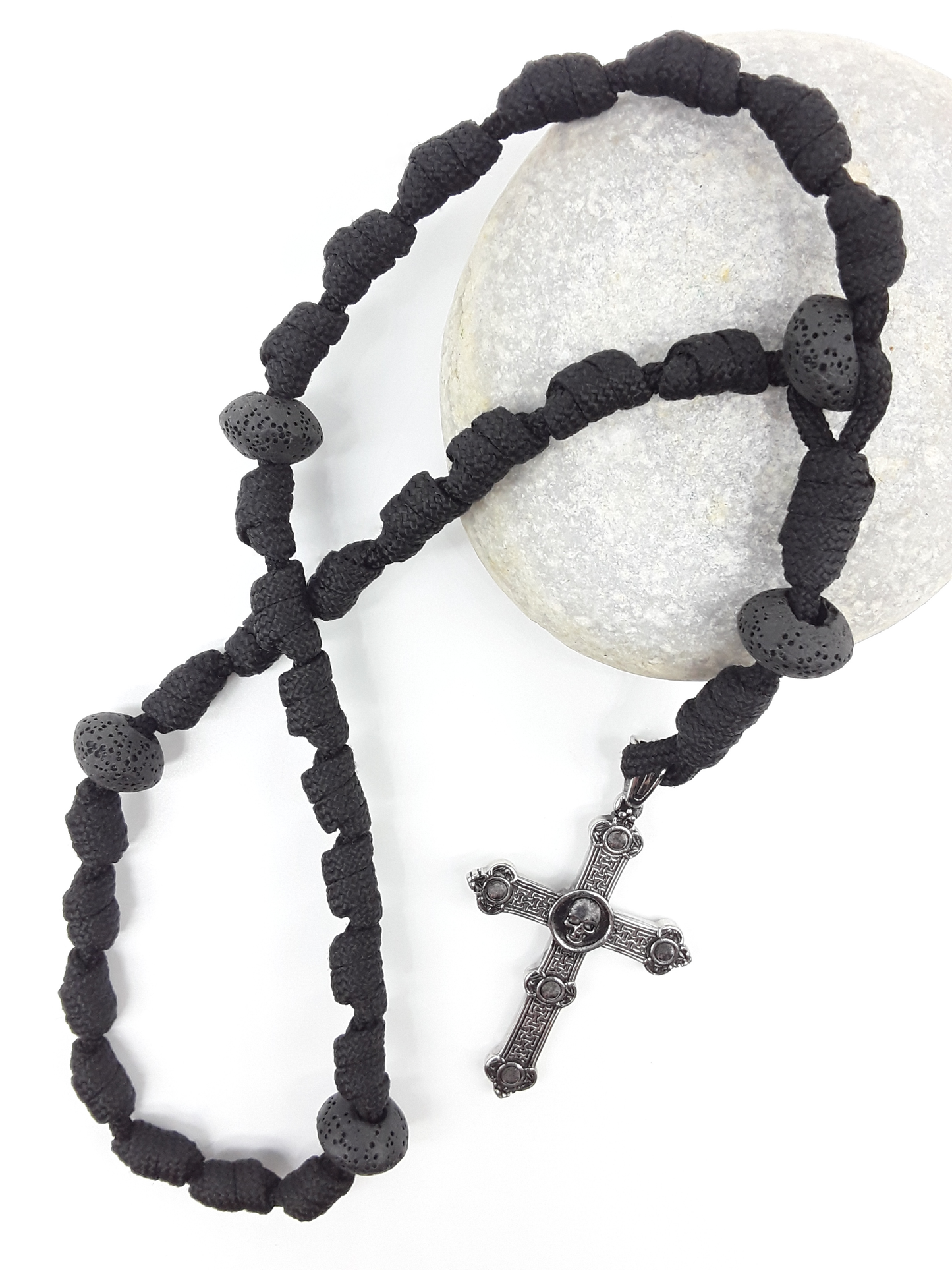 The Living Memory Paracord Anglican Prayer Beads by Polmadeva placed on stone, crafted with Volcanic Lava Stones and stainless steel Skull Cross