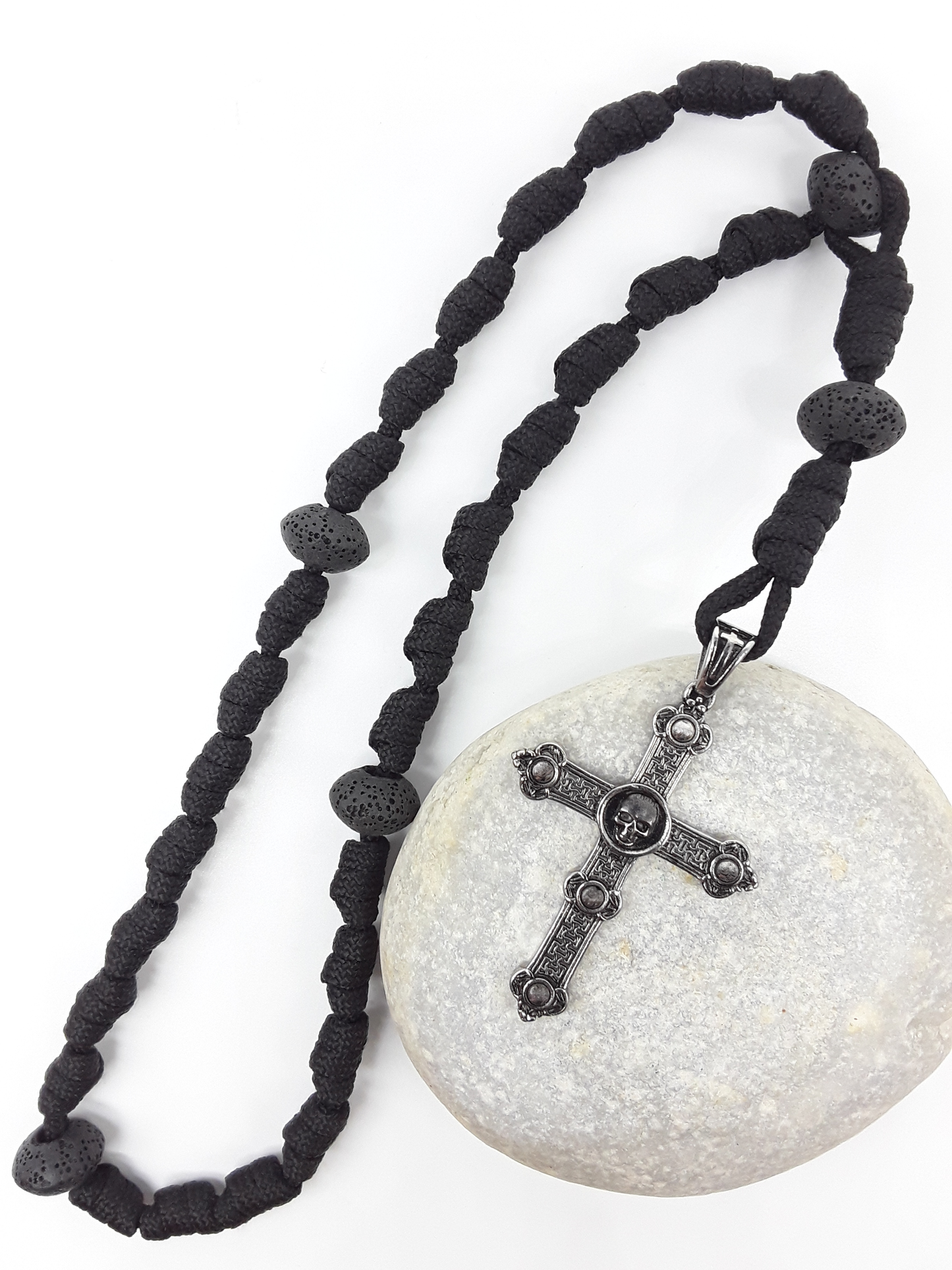 The Living Memory Paracord Anglican Prayer Beads by Polmadeva placed on stone, crafted with Volcanic Lava Stones and stainless steel Skull Cross