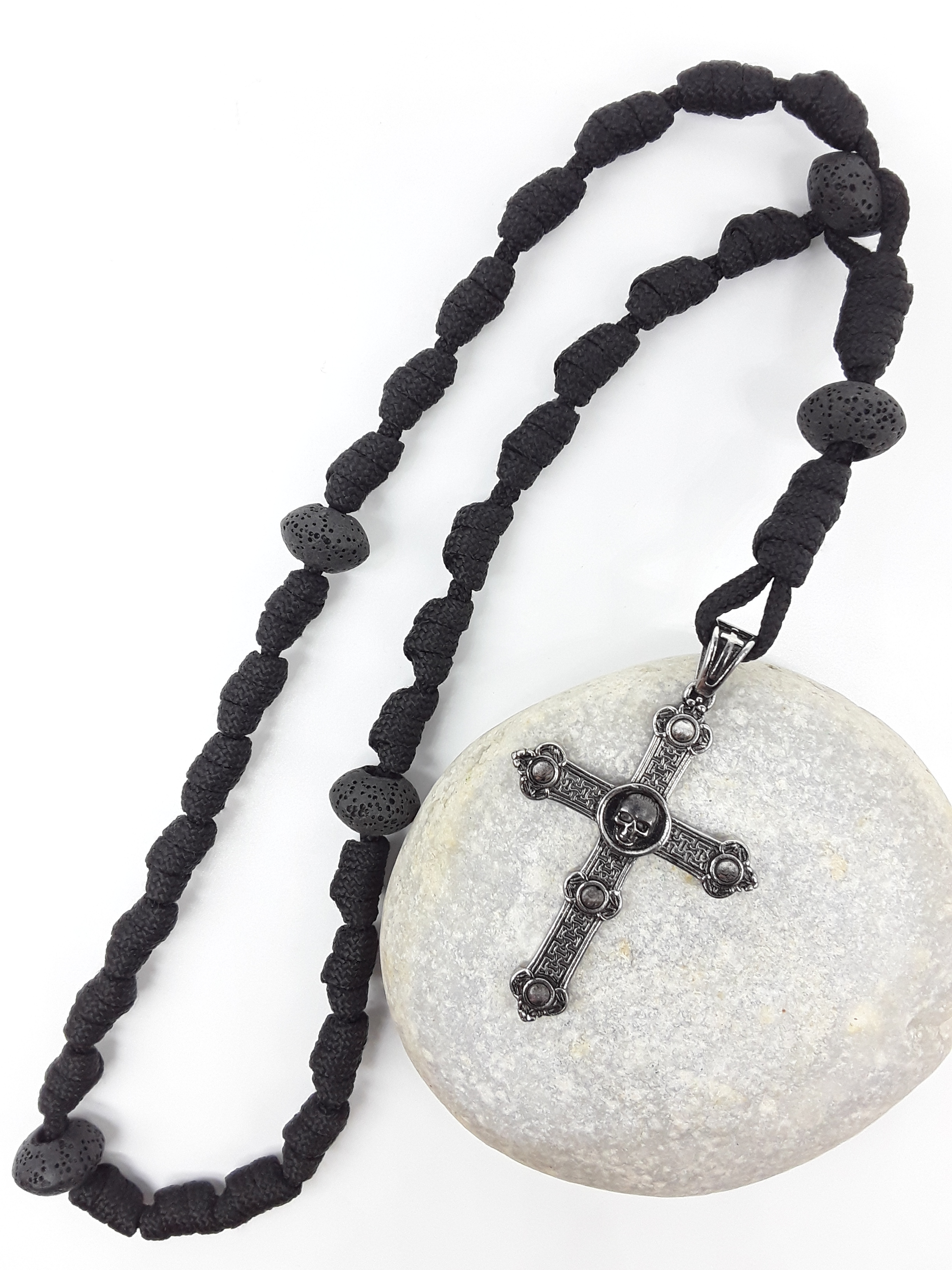 The Living Memory Paracord Anglican Prayer Beads by Polmadeva placed on stone, crafted with Volcanic Lava Stones and stainless steel Skull Cross