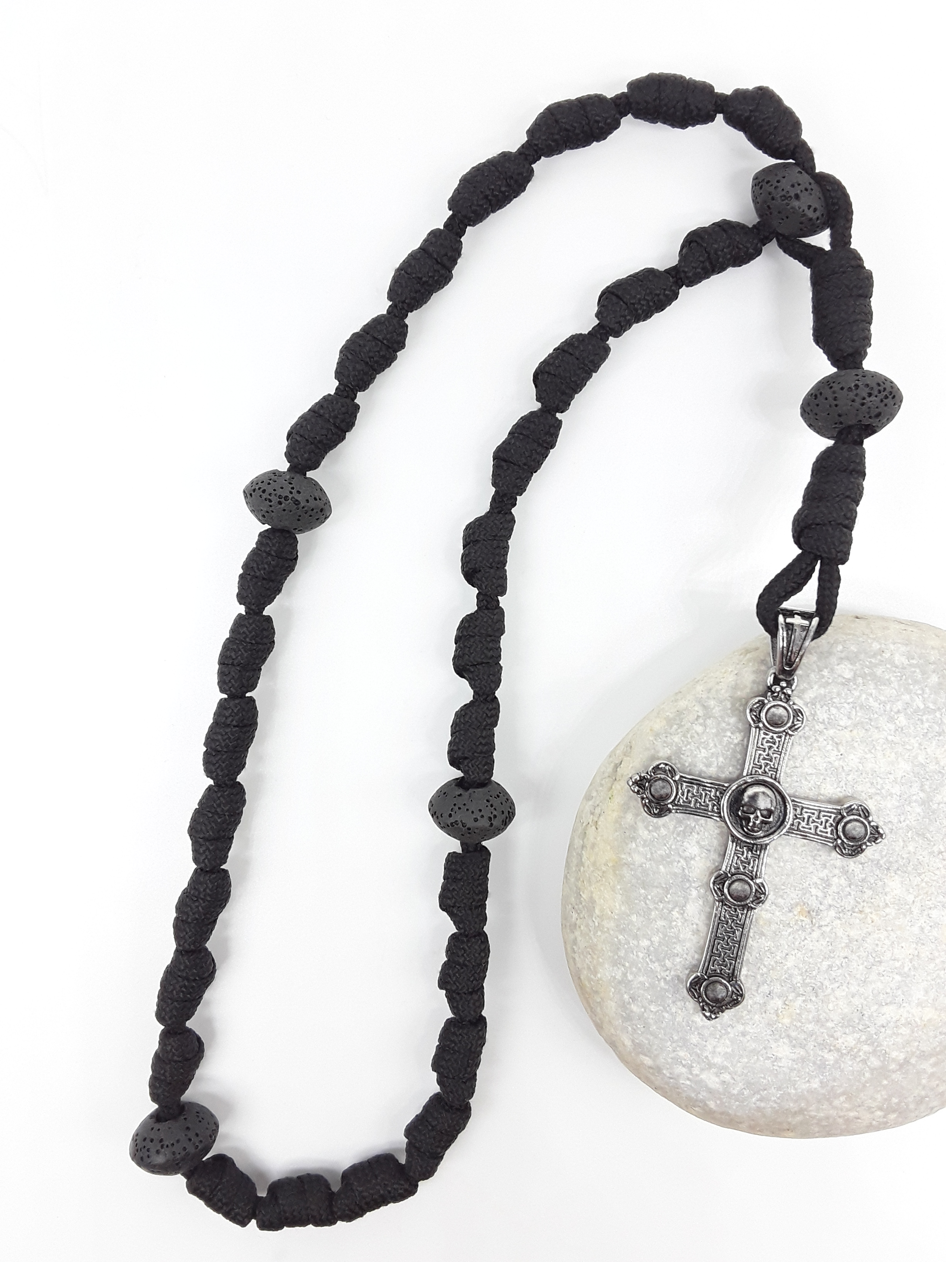 The Living Memory Paracord Anglican Prayer Beads by Polmadeva placed on stone, crafted with Volcanic Lava Stones and stainless steel Skull Cross