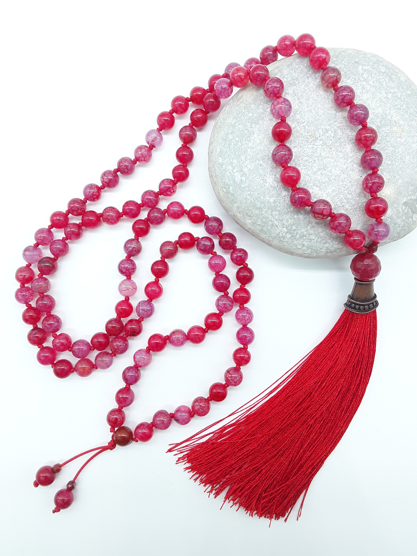 Dragon Veins Agate Mala Beads with red tassel placed on white stone on white background, Polmadeva