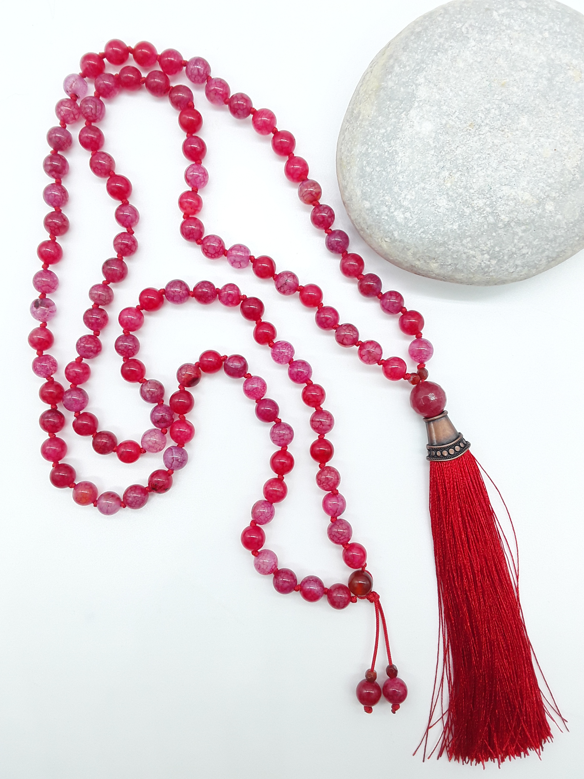 Dragon Veins Agate Mala Beads with red tassel placed beside white stone on white background, Polmadeva