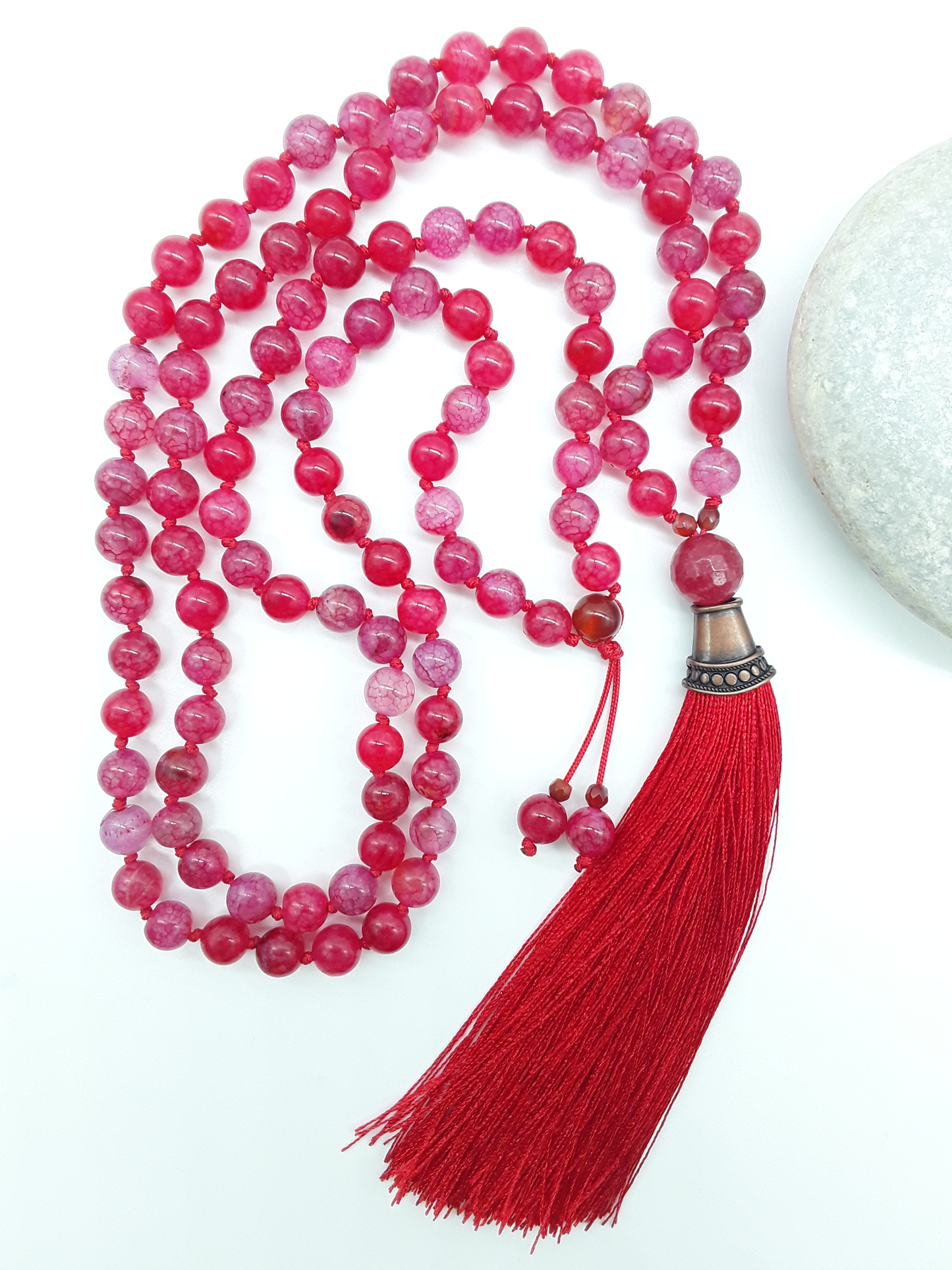 Dragon Veins Agate Mala Beads with red tassel placed beside white stone on white background, Polmadeva