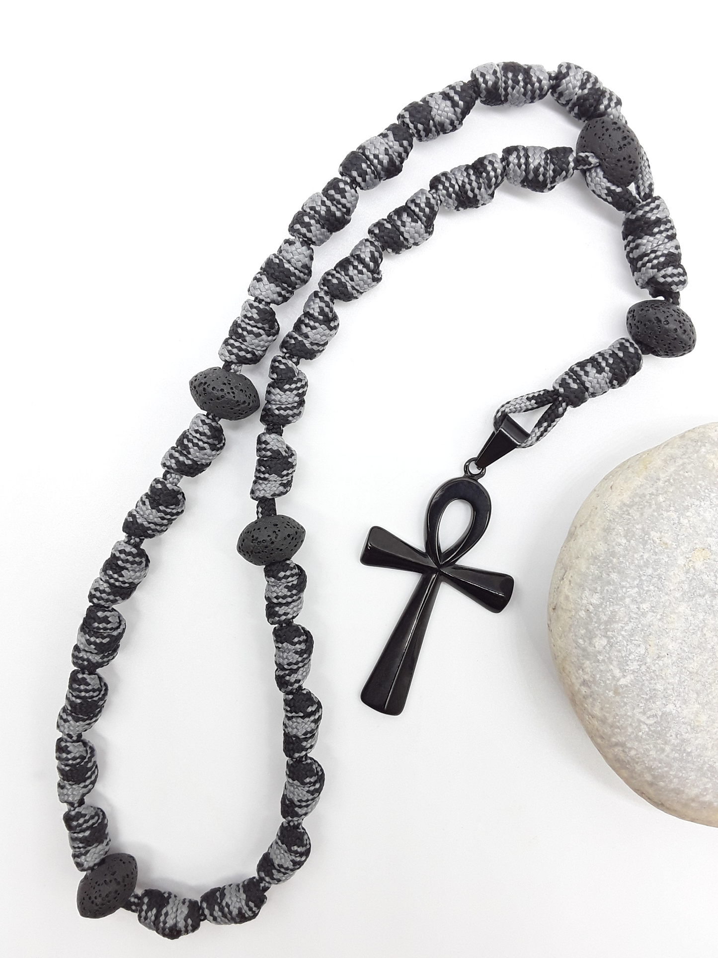 The Living Thread Paracord Anglican Prayer Beads by Polmadeva beside natural stone, featuring Lava Stones and stainless steel Ankh Cross