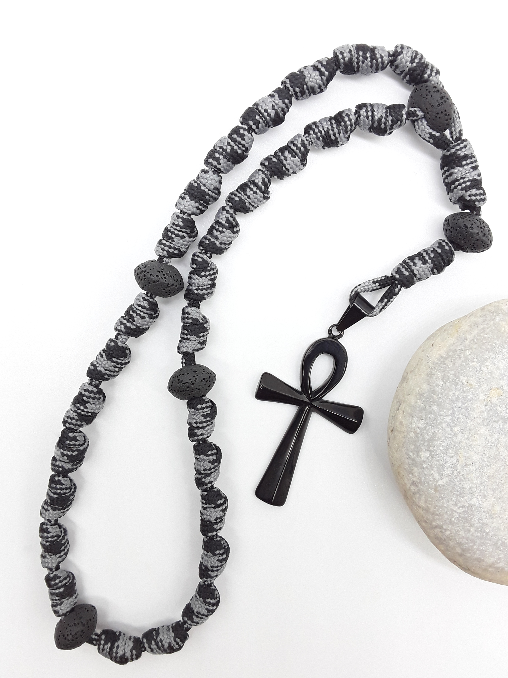The Living Thread Paracord Anglican Prayer Beads by Polmadeva beside natural stone, featuring Lava Stones and stainless steel Ankh Cross
