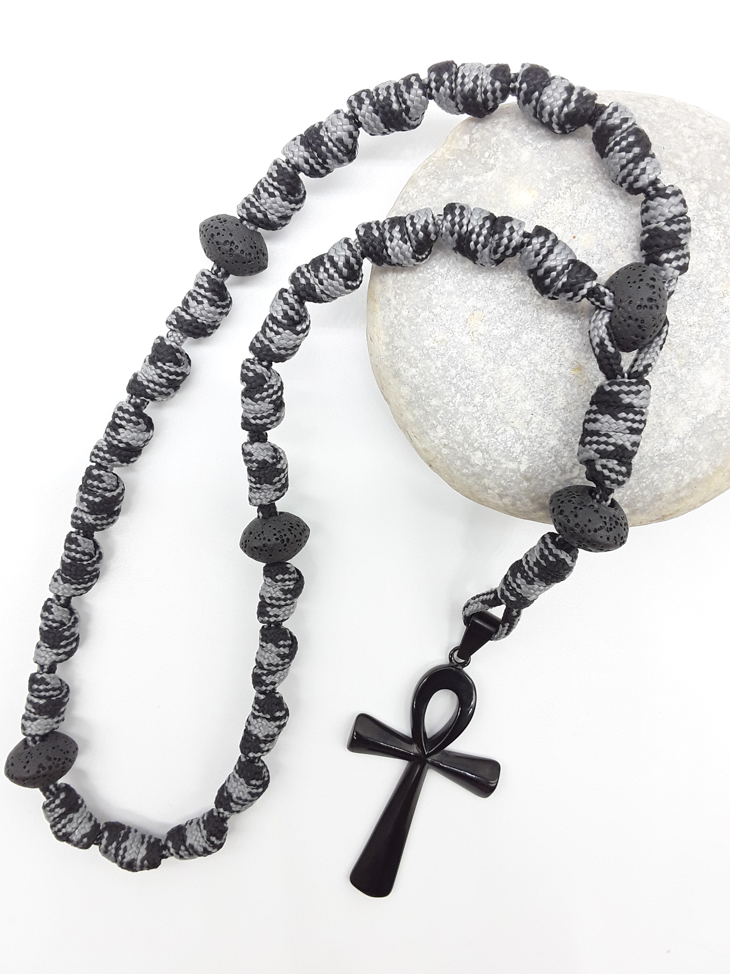 The Living Thread Paracord Anglican Prayer Beads by Polmadeva placed on stone, crafted with Lava Stones and stainless steel Ankh Cross