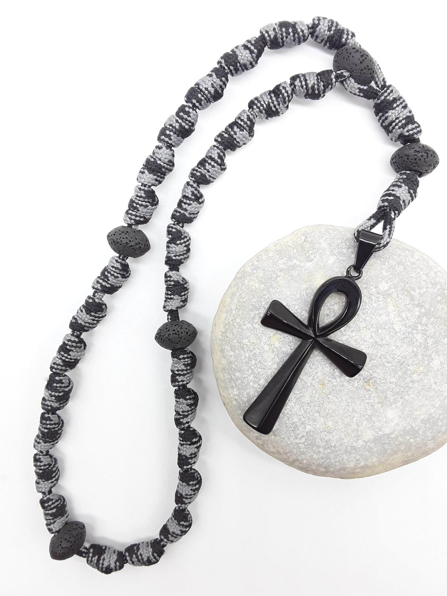 The Living Thread Paracord Anglican Prayer Beads by Polmadeva placed on stone, crafted with Lava Stones and stainless steel Ankh Cross