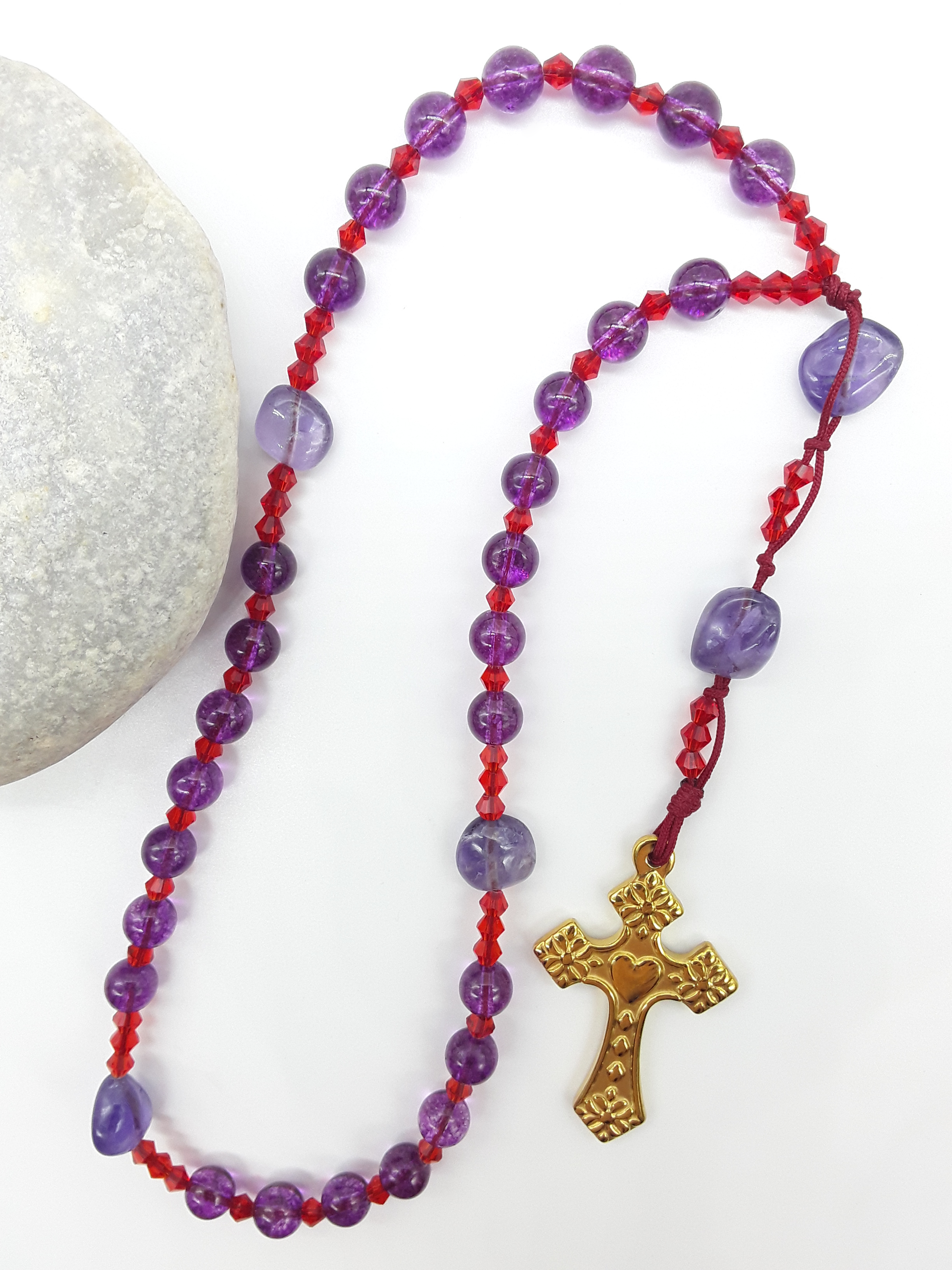 The Luminous Offering Anglican Prayer Beads by Polmadeva beside natural stone, featuring Amethyst, Purple Quartz, Swarovski crystals, and gold-tone cross