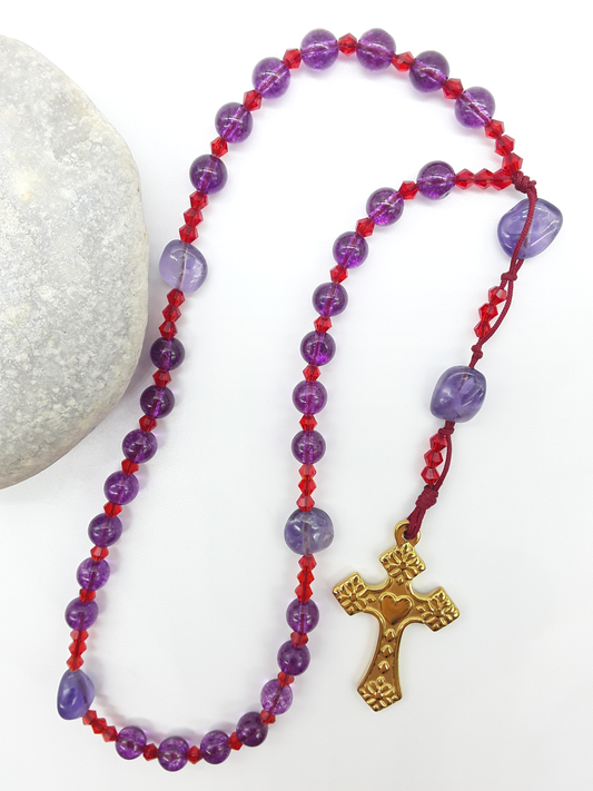 The Luminous Offering Anglican Prayer Beads by Polmadeva beside natural stone, featuring Amethyst, Purple Quartz, Swarovski crystals, and gold-tone cross