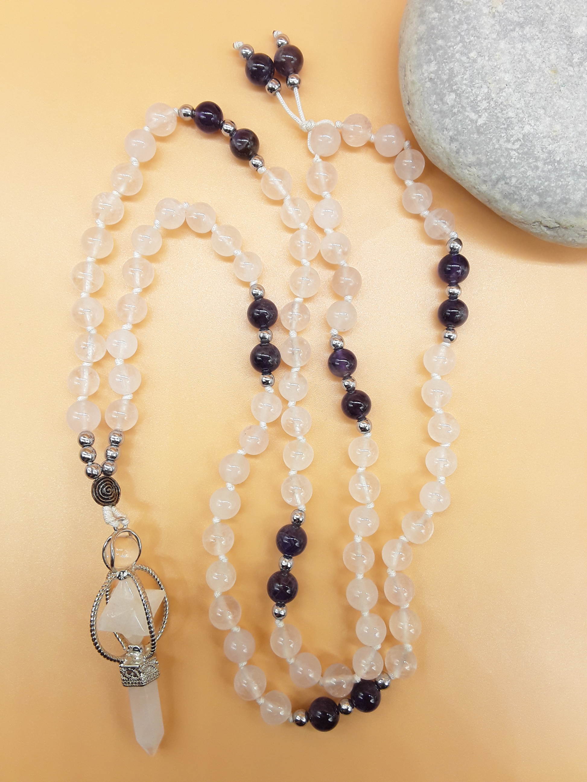 Quartz and Amethyst Mala Beads with Natural Quartz Crystal pendant placed beside white stone on soft background, Polmadeva
