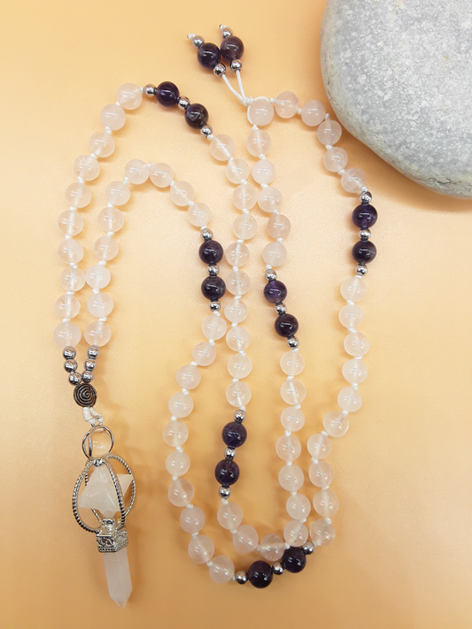 Quartz and Amethyst Mala Beads with Natural Quartz Crystal pendant placed beside white stone on soft background, Polmadeva