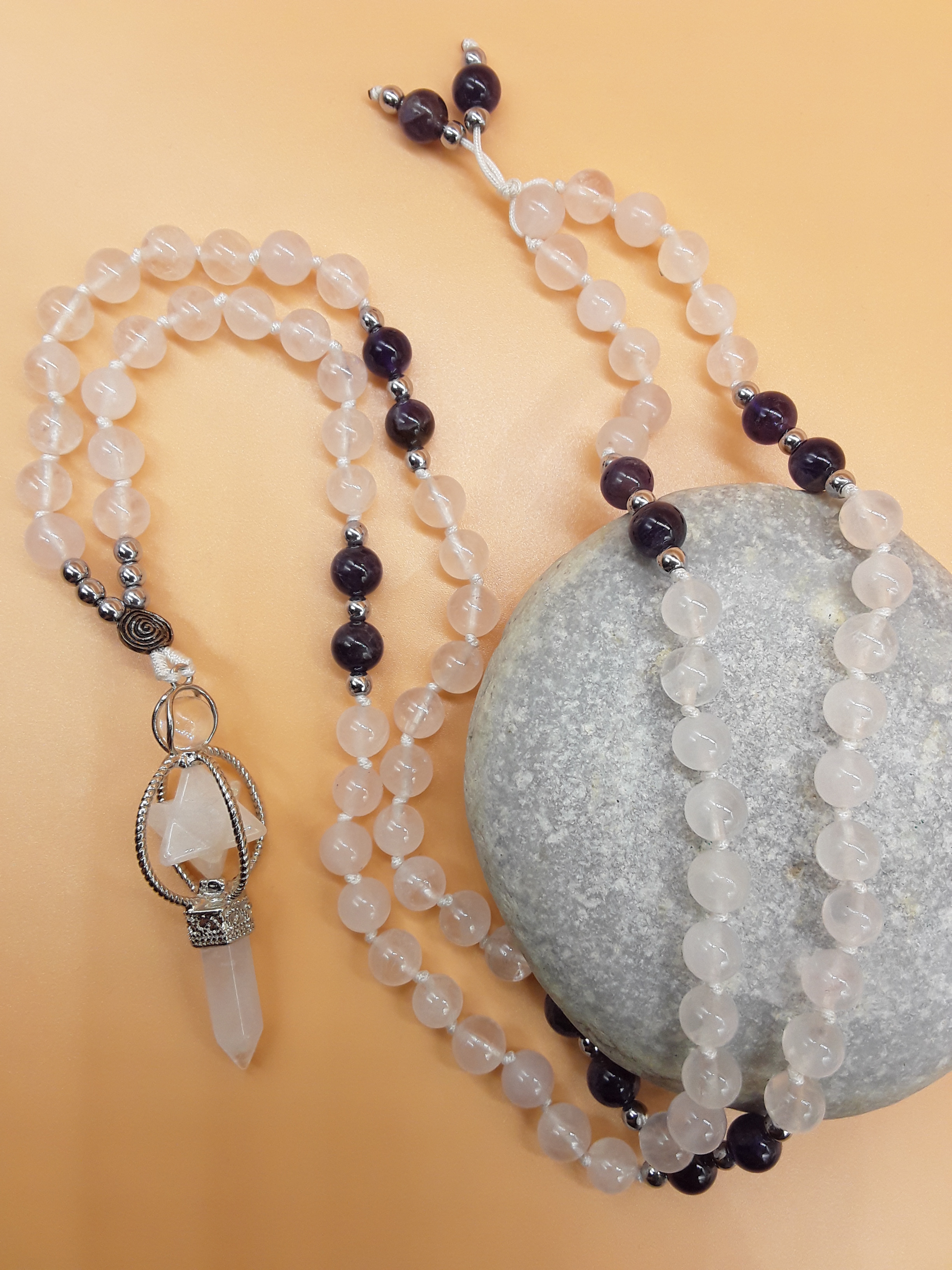 Quartz and Amethyst Mala Beads with Natural Quartz Crystal pendant placed om white stone on soft background, Polmadeva