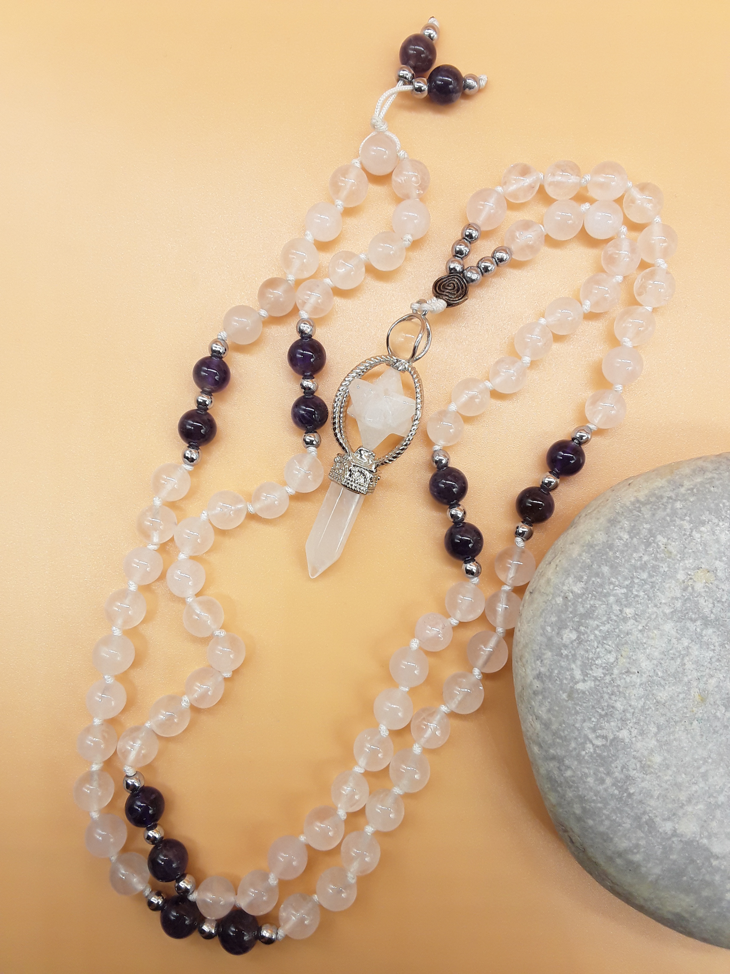 Quartz and Amethyst Mala Beads with Natural Quartz Crystal pendant placed beside white stone on soft background, Polmadeva