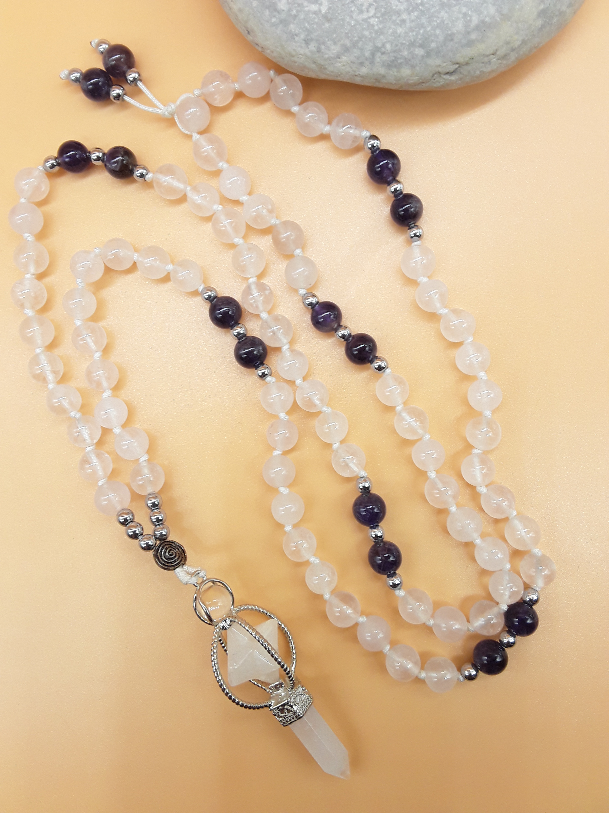 Quartz and Amethyst Mala Beads with Natural Quartz Crystal pendant placed beside white stone on soft background, Polmadeva