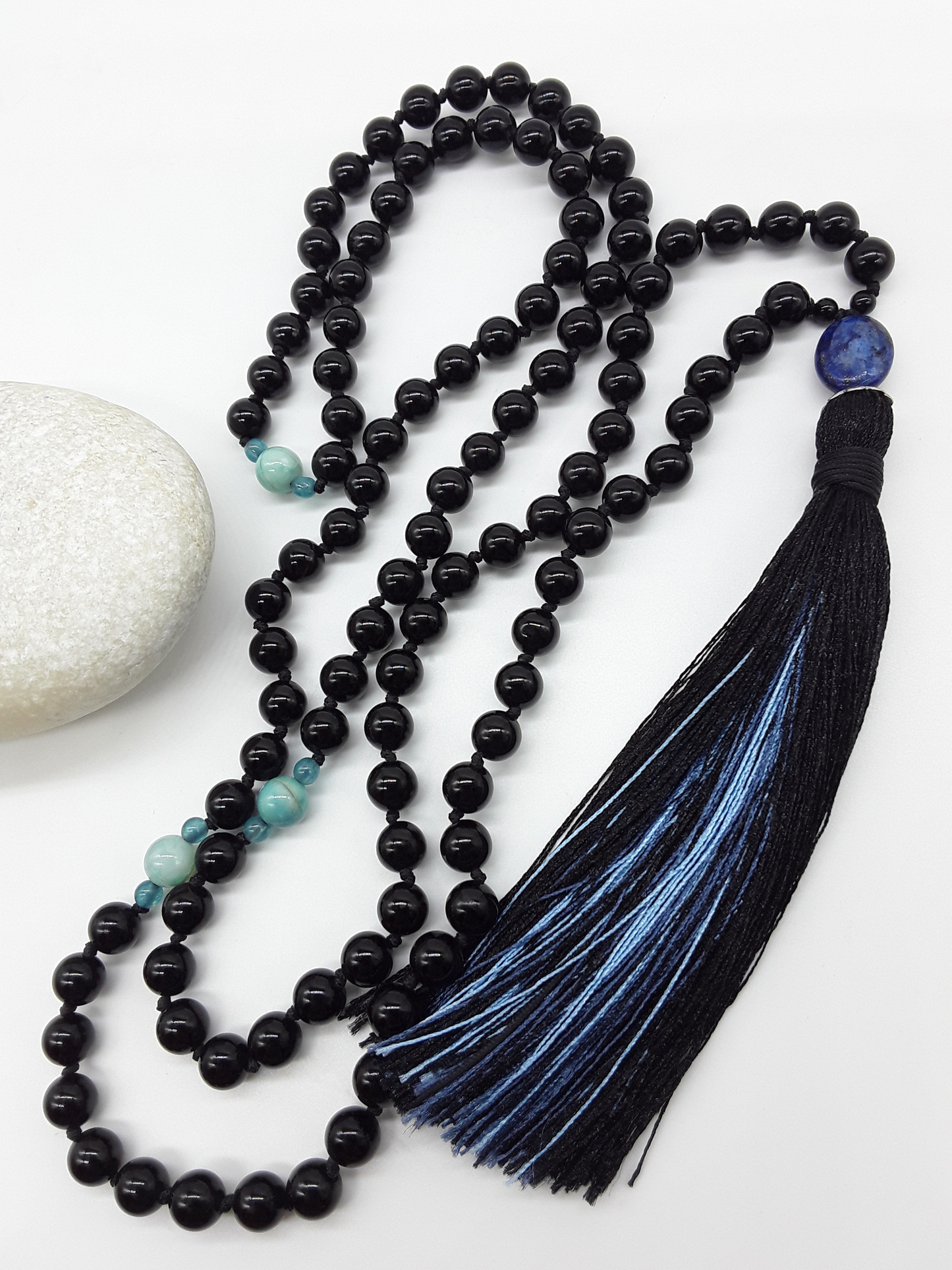 Black Onyx Mala Beads with Lapis Lazuli, Agate accents and tassel placed beside white stone on white background, Polmadeva