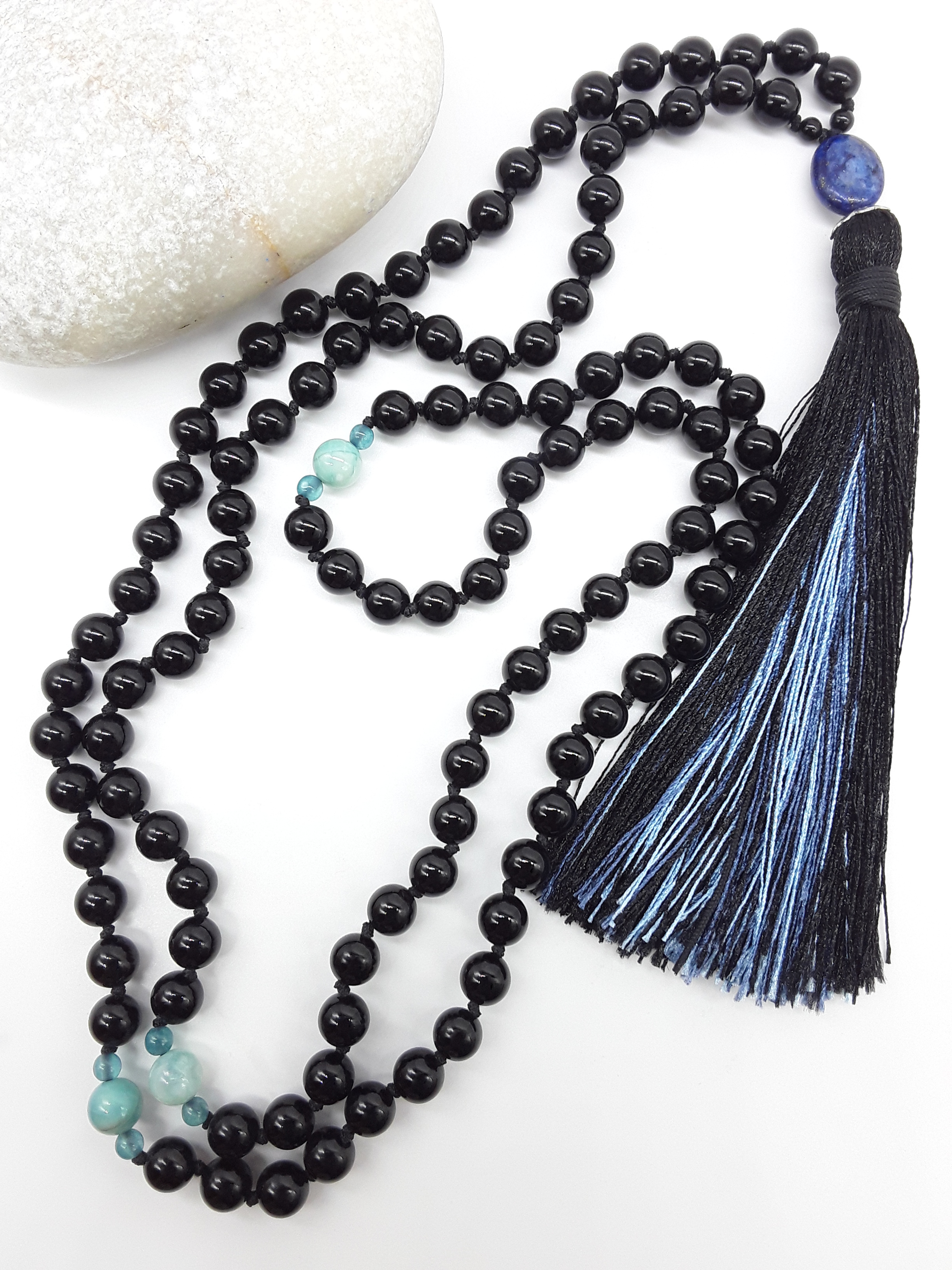 Black Onyx Mala Beads with Lapis Lazuli, Agate accents and tassel placed beside white stone on white background, Polmadeva