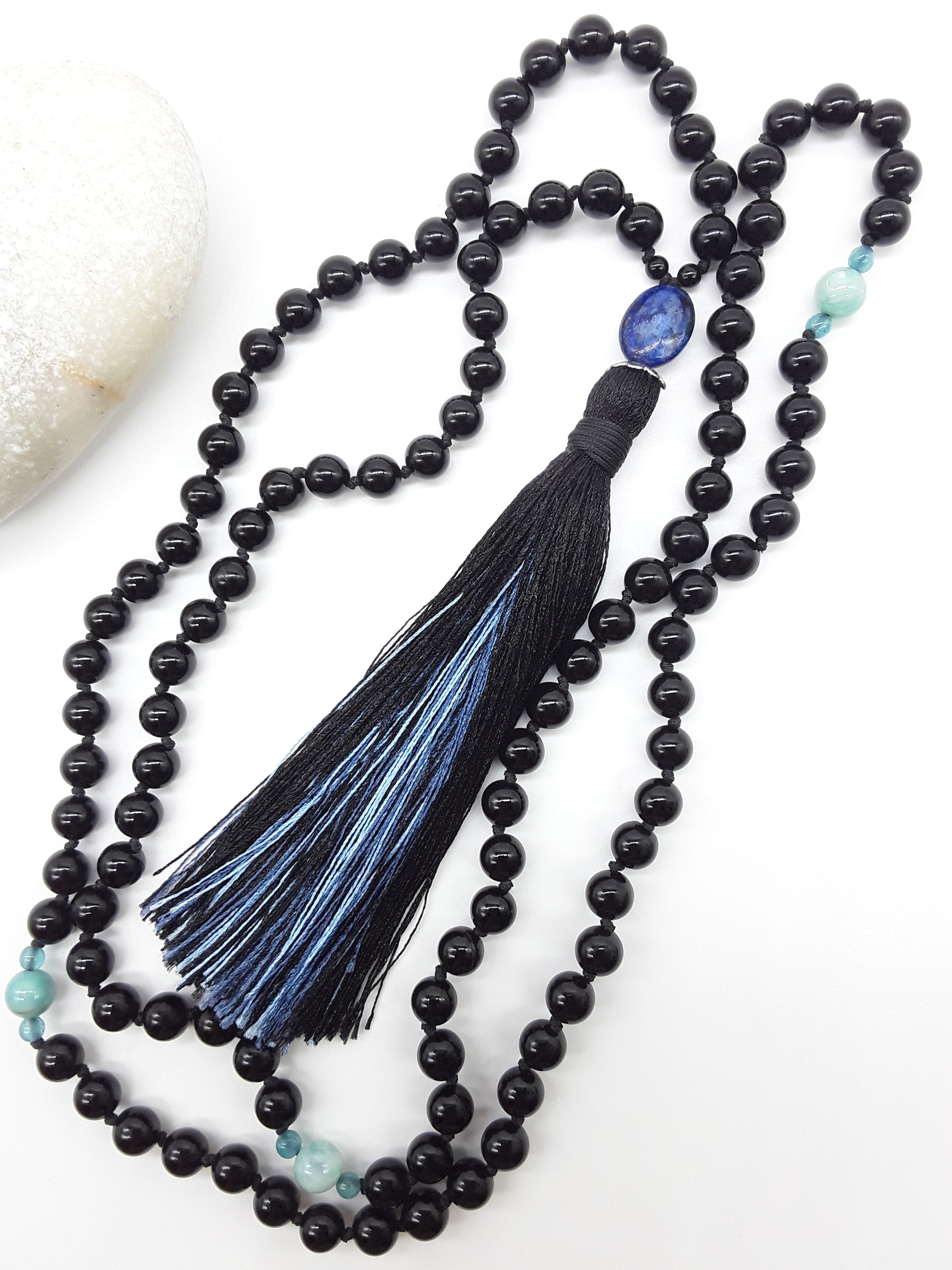 Black Onyx Mala Beads with Lapis Lazuli, Agate accents and tassel placed beside white stone on white background, Polmadeva