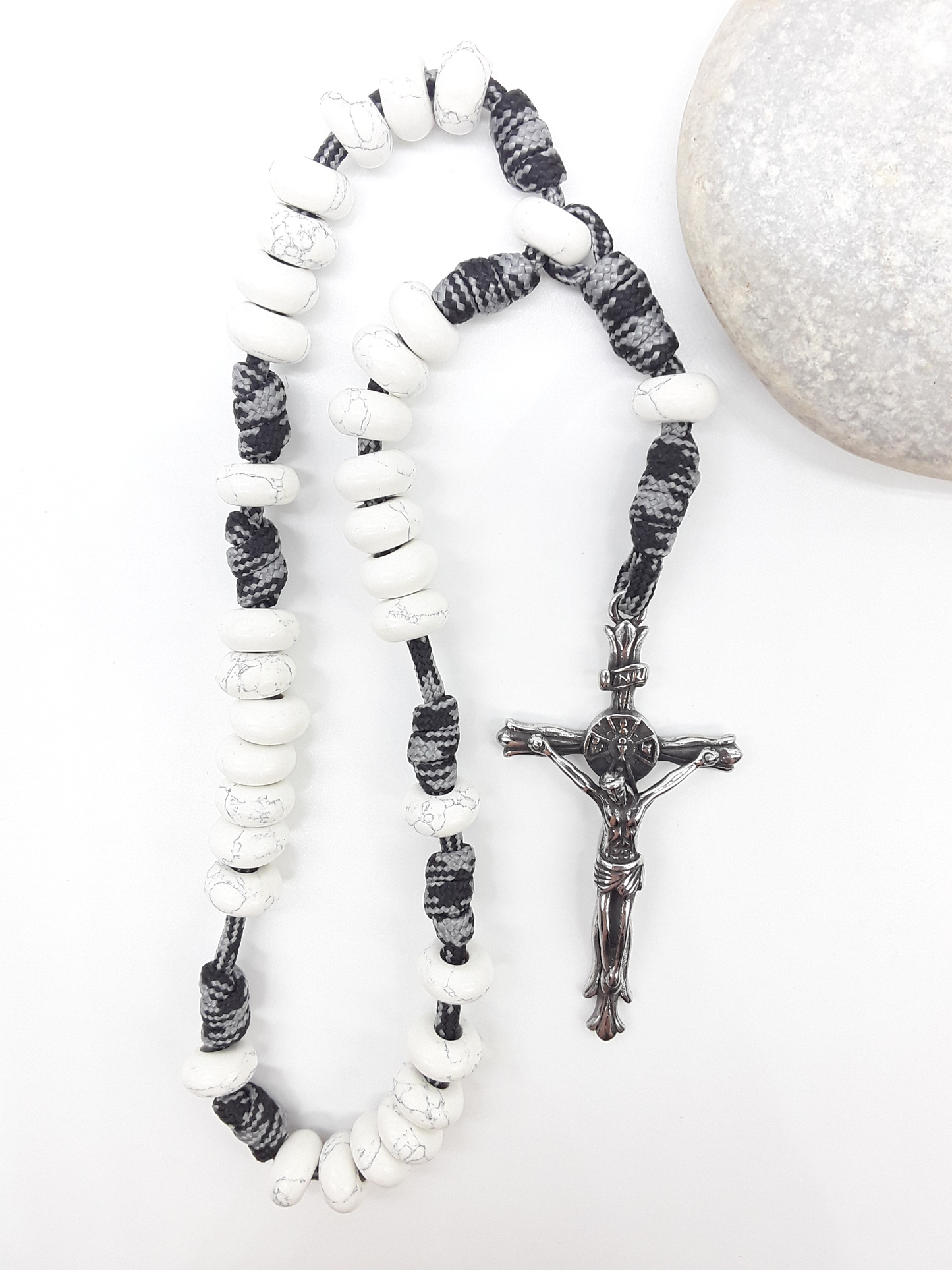 The Quiet Contrast Paracord Anglican Prayer Beads by Polmadeva beside natural stone, featuring Howlite and crucifix