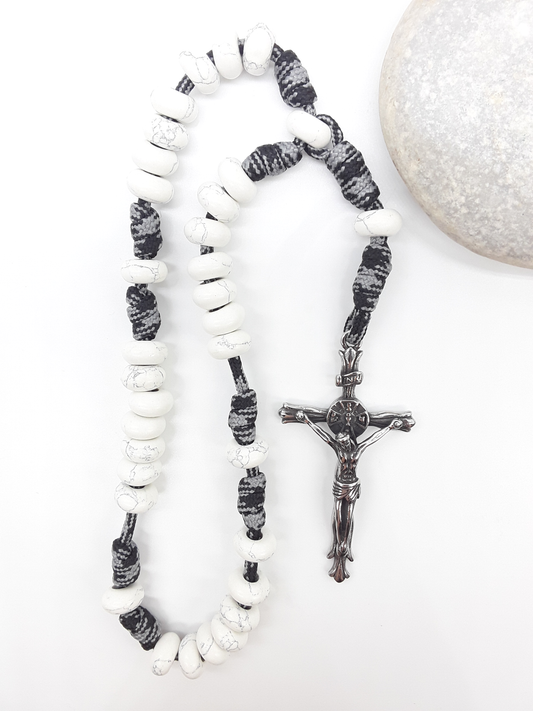 The Quiet Contrast Paracord Anglican Prayer Beads by Polmadeva beside natural stone, featuring Howlite and crucifix