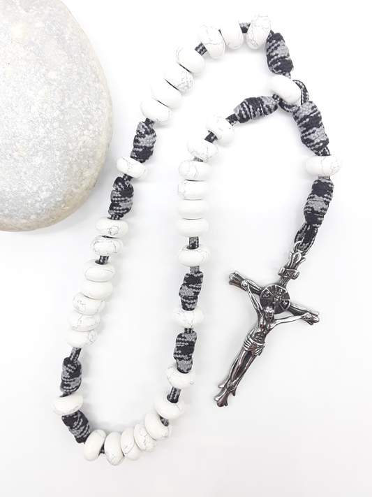 The Quiet Contrast Paracord Anglican Prayer Beads by Polmadeva beside natural stone, featuring Howlite and crucifix