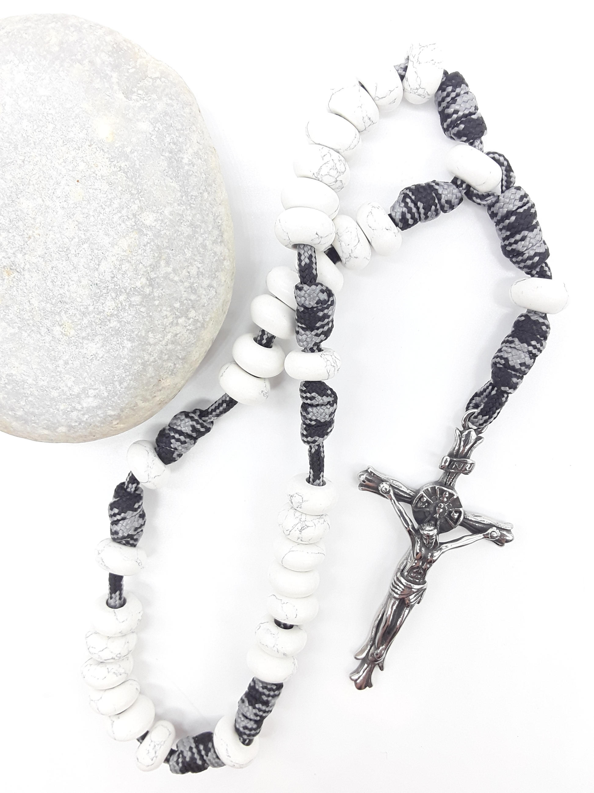The Quiet Contrast Paracord Anglican Prayer Beads by Polmadeva beside natural stone, featuring Howlite and crucifix