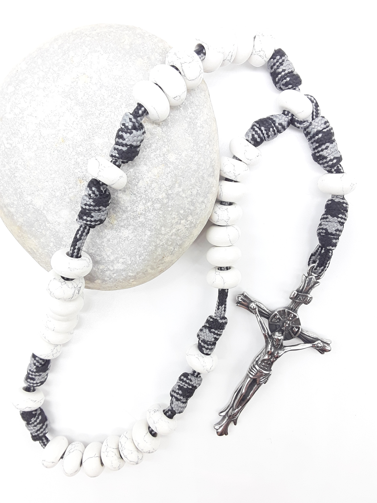 The Quiet Contrast Paracord Anglican Prayer Beads by Polmadeva placed on stone, crafted with Howlite and stainless steel crucifix
