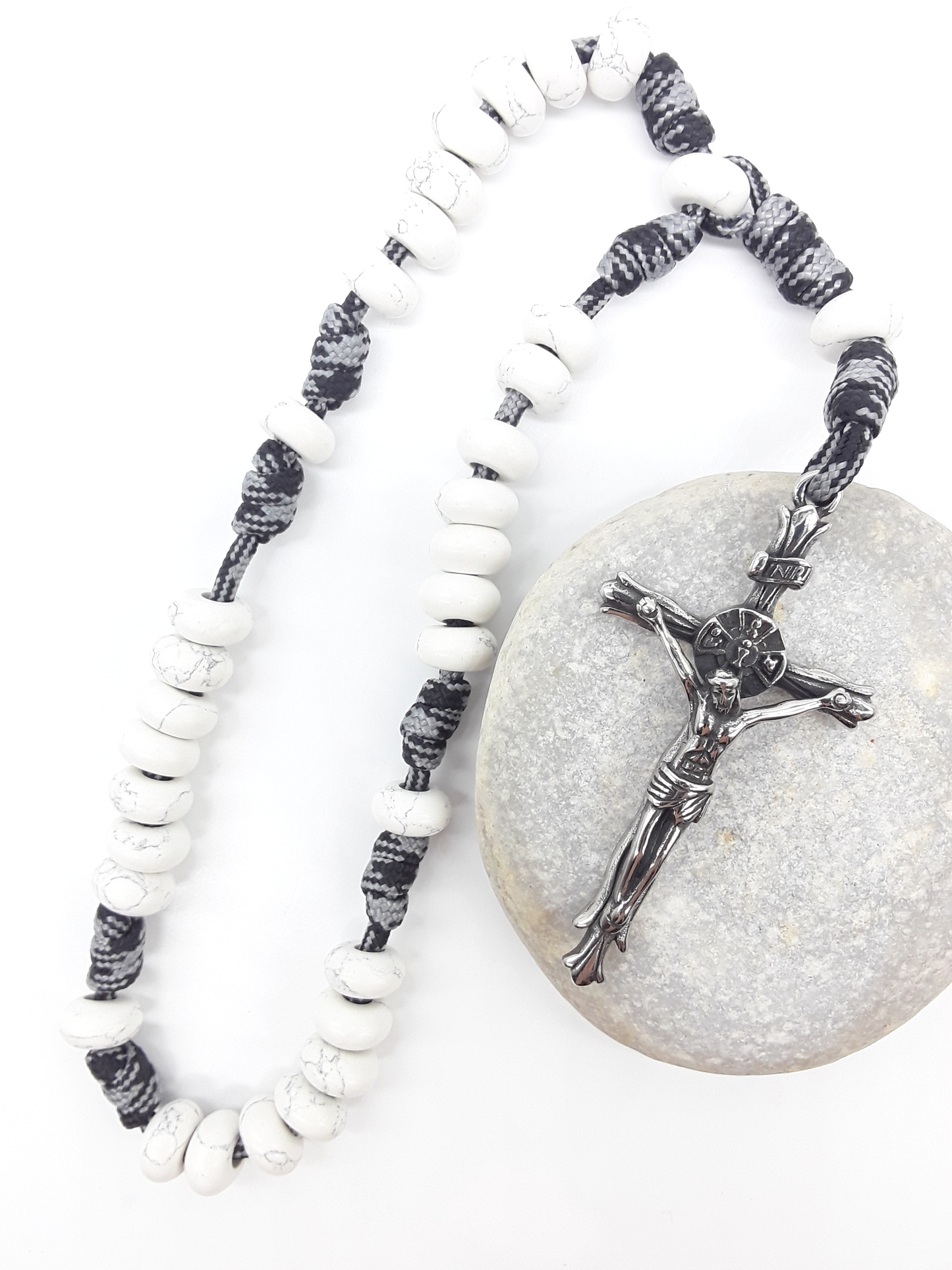 The Quiet Contrast Paracord Anglican Prayer Beads by Polmadeva placed on stone, crafted with Howlite and stainless steel crucifix