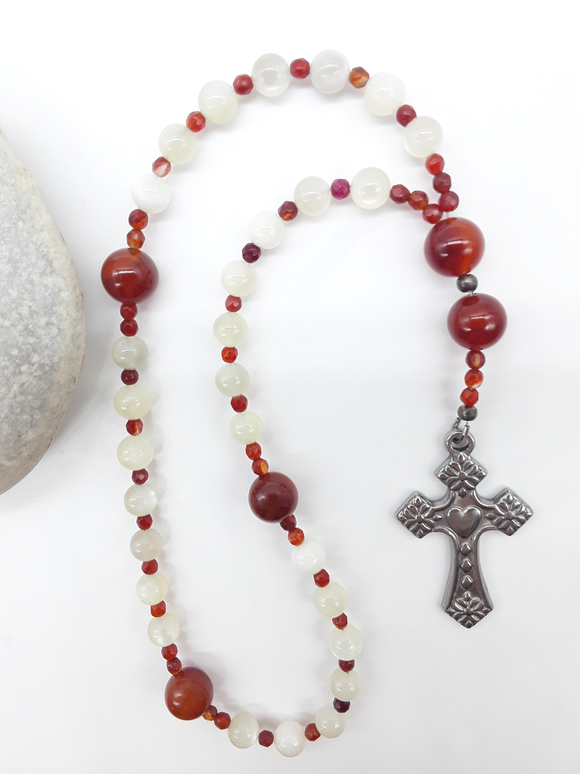 The Quiet Flame Anglican Prayer Beads by Polmadeva beside natural stone, featuring Carnelian, Moonstone, Agate, and stainless steel cross