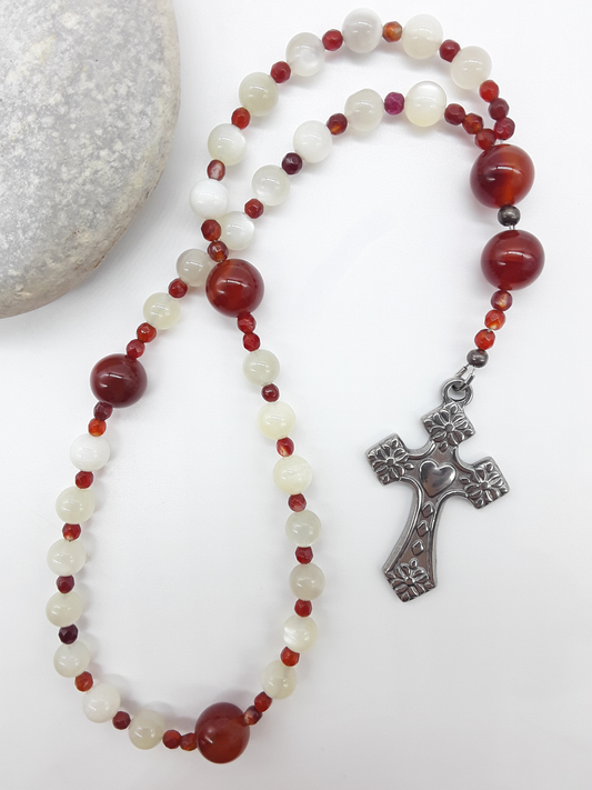 The Quiet Flame Anglican Prayer Beads by Polmadeva beside natural stone, featuring Carnelian, Moonstone, Agate, and stainless steel cross