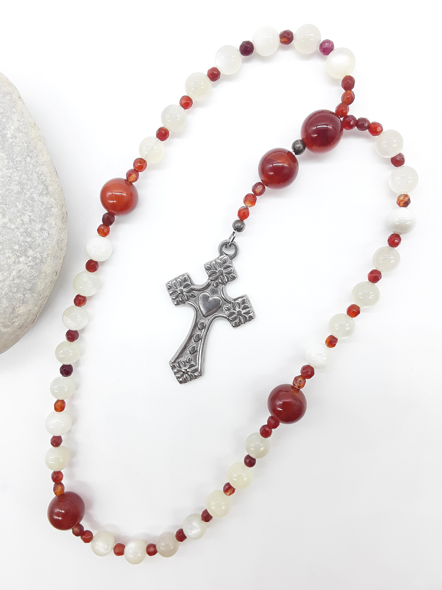 The Quiet Flame Anglican Prayer Beads by Polmadeva beside natural stone, featuring Carnelian, Moonstone, Agate, and stainless steel cross