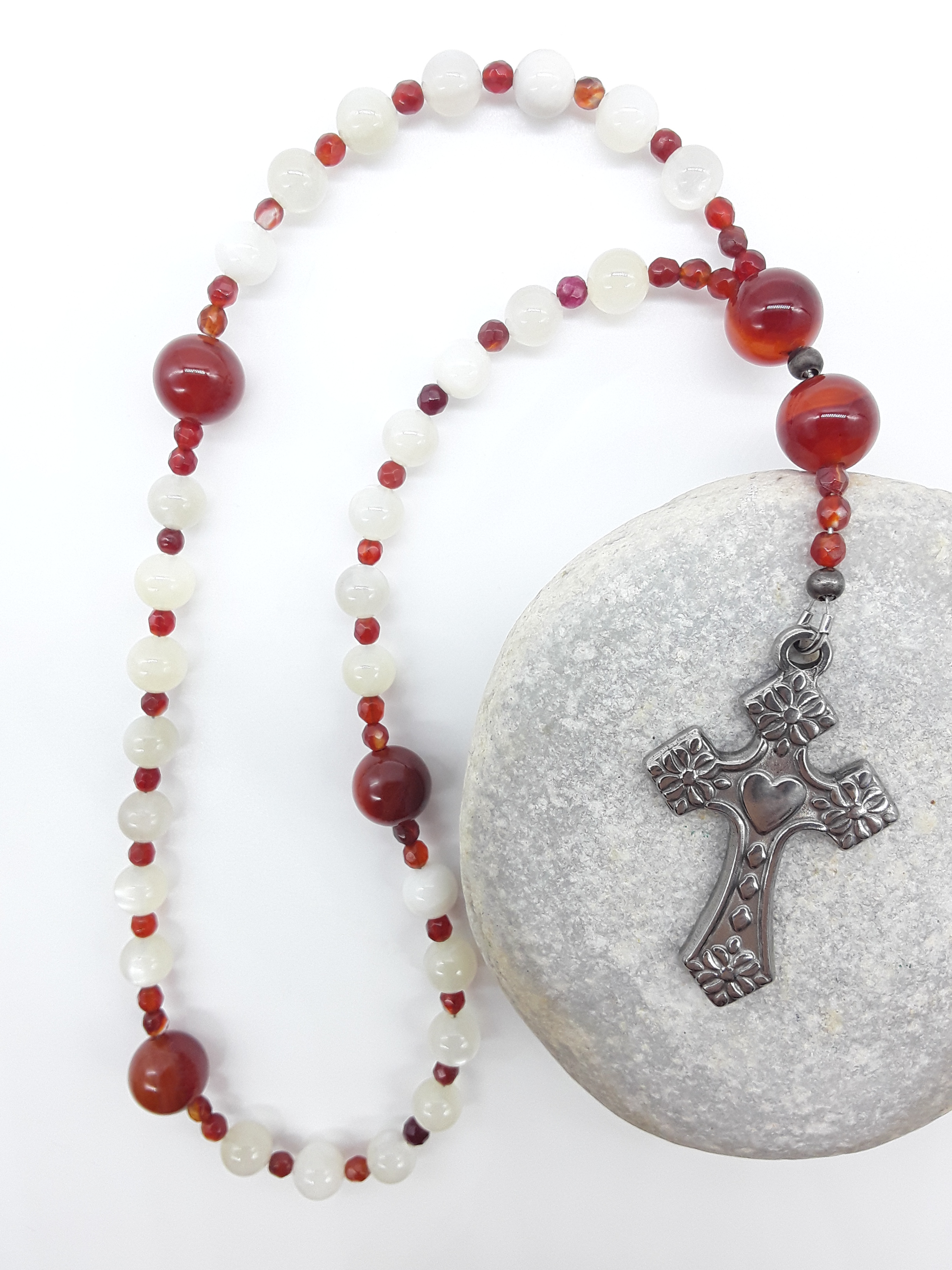 The Quiet Flame Anglican Prayer Beads by Polmadeva placed on stone, crafted with Carnelian, Moonstone, Agate, and stainless steel cross