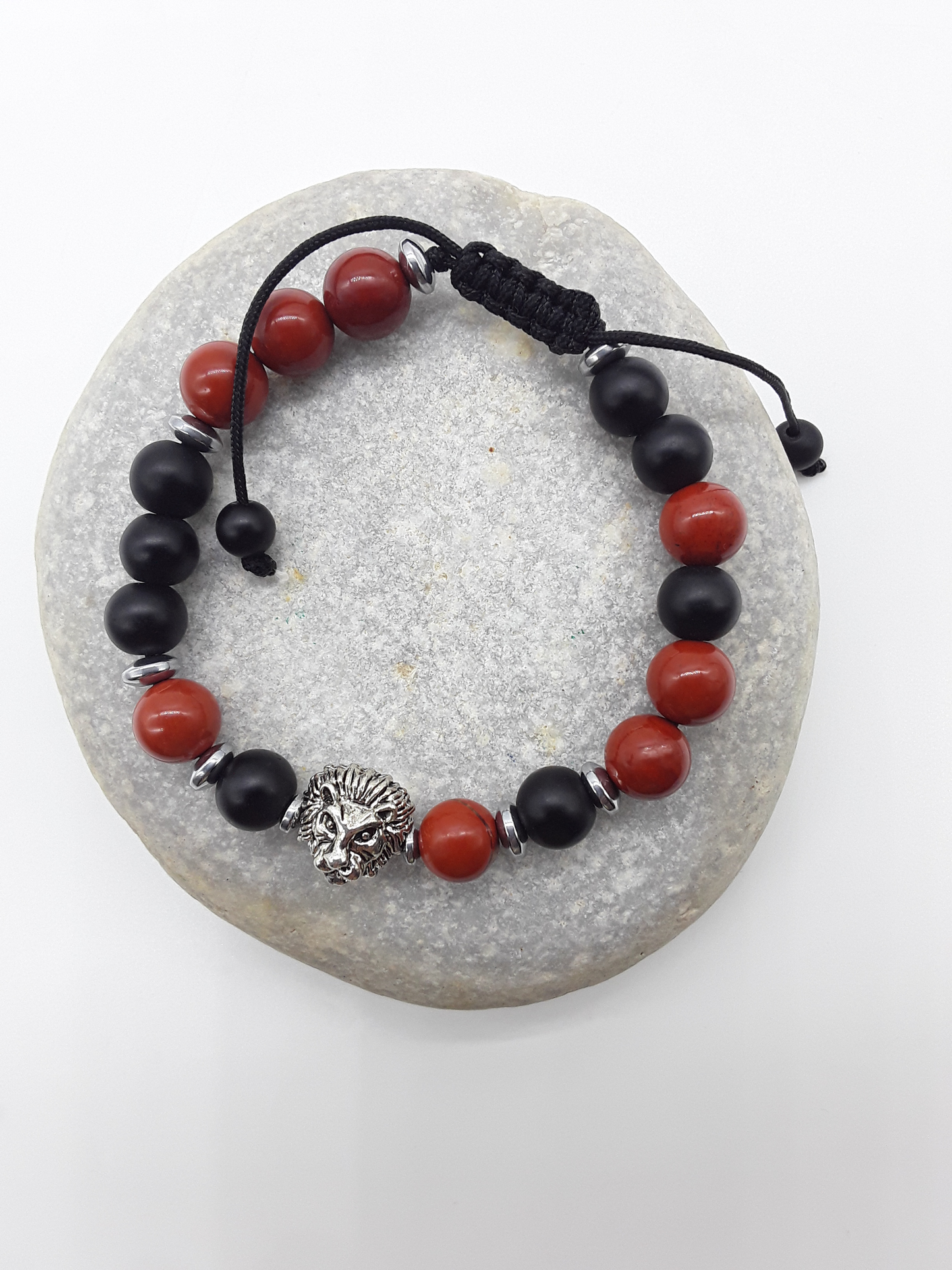 The Quiet Hold Lion Bracelet by Polmadeva resting on natural stone, featuring red jasper, matte onyx and hematite