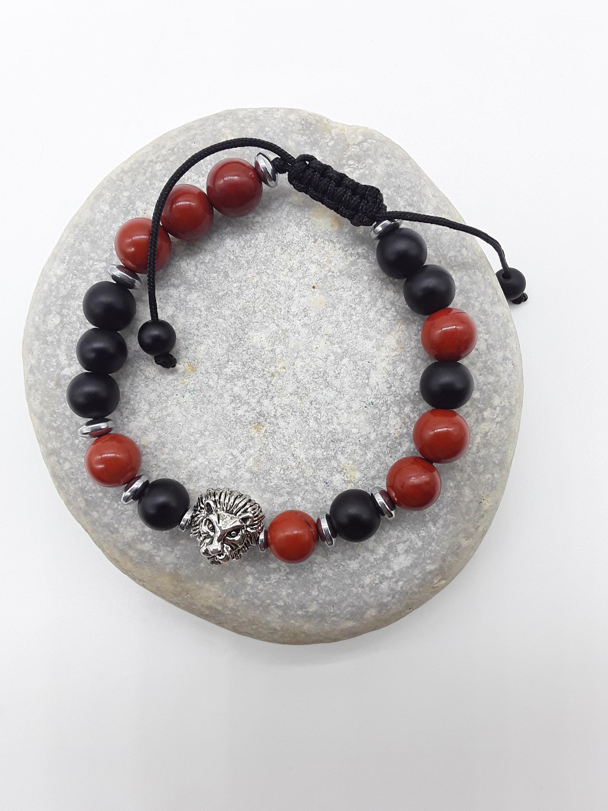 The Quiet Hold Lion Bracelet by Polmadeva resting on natural stone, featuring red jasper, matte onyx and hematite