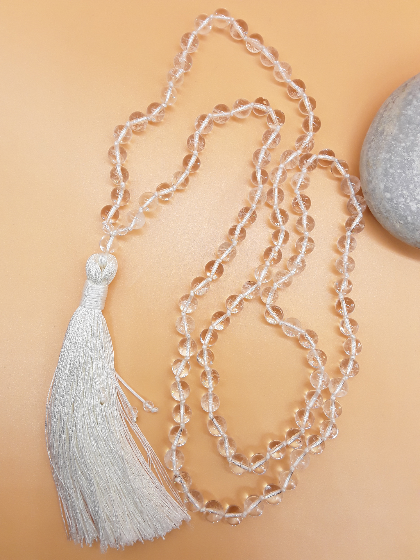 Crystal Quartz Mala Beads with white tassel placed beside white stone on soft background, Polmadeva