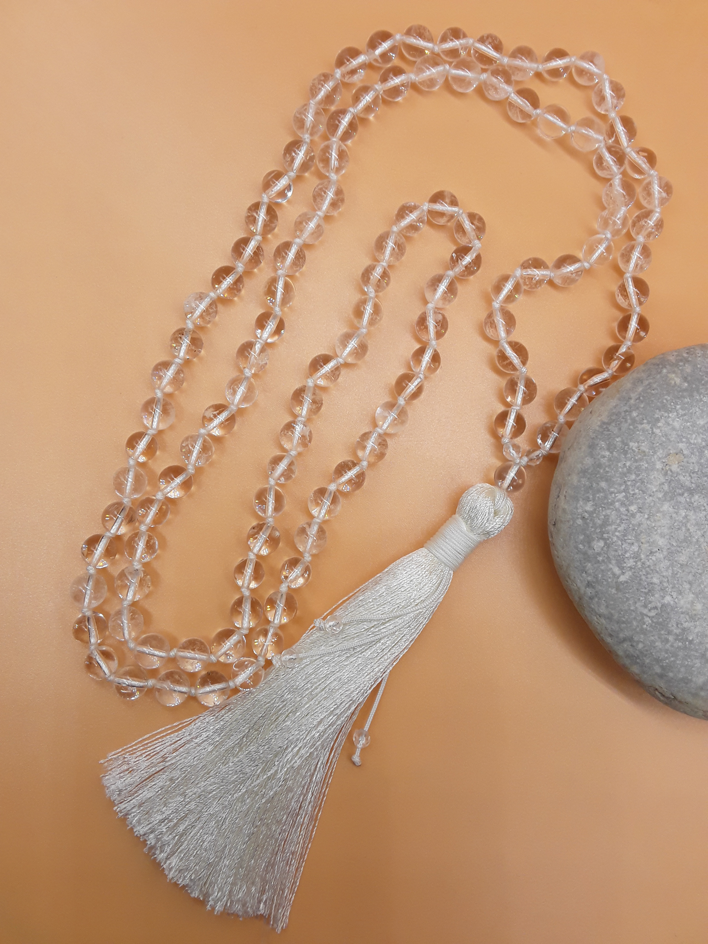 Crystal Quartz Mala Beads with white tassel placed beside white stone on soft background, Polmadeva