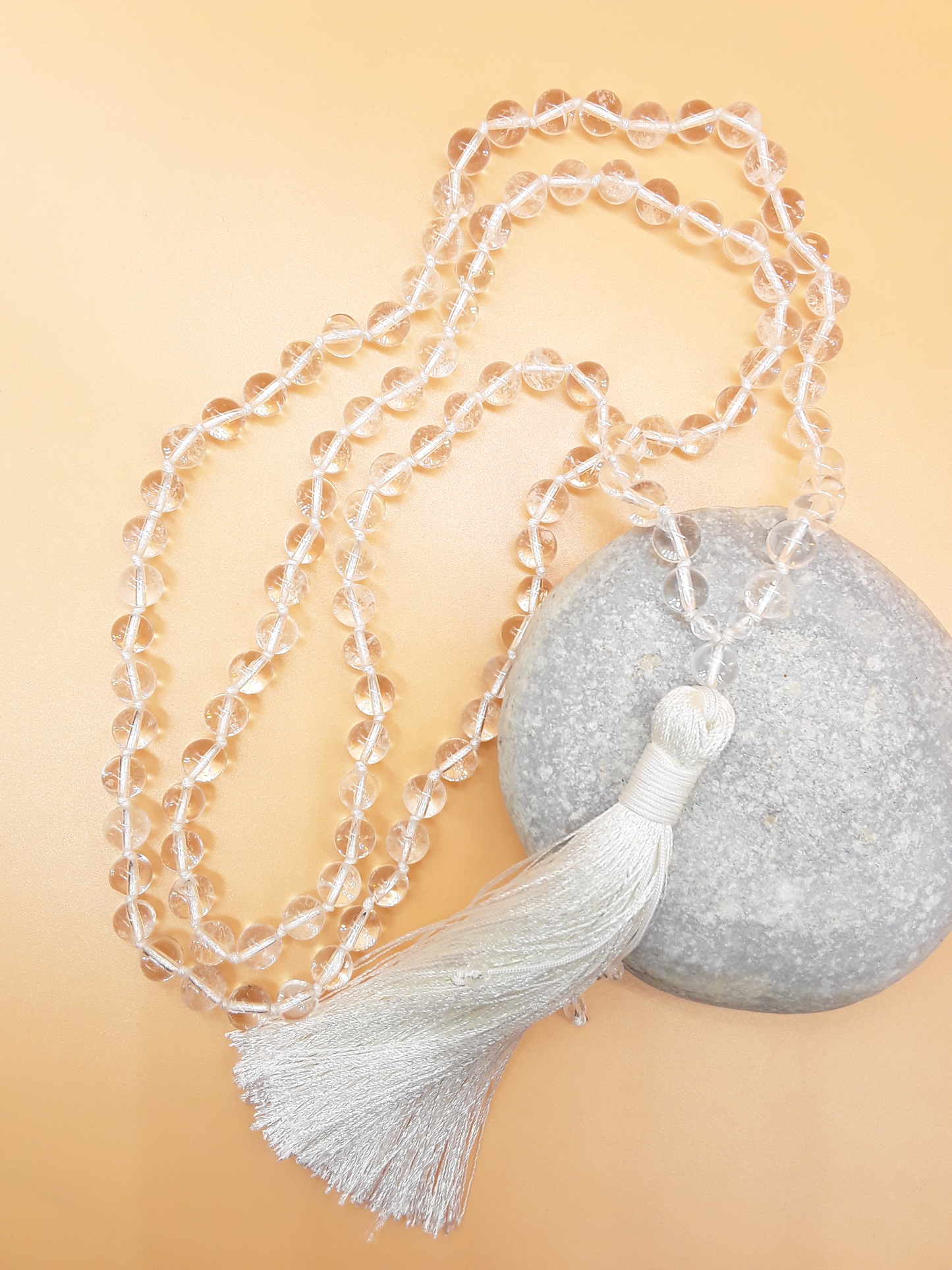 Crystal Quartz Mala Beads with white tassel placed beside white stone on soft background, Polmadeva
